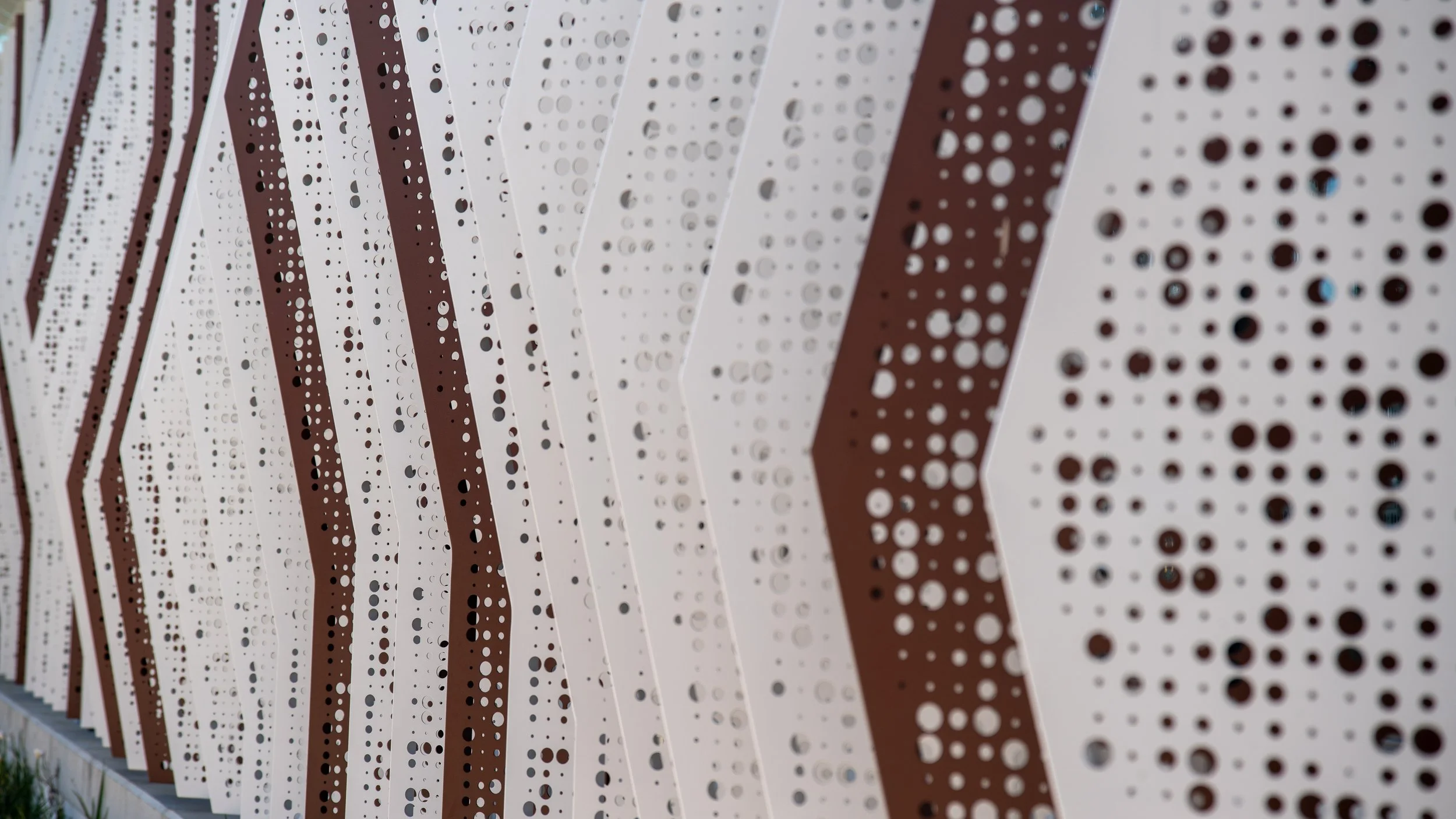 Close-up of a modern metal wall with alternating white and brown panels, each featuring circular perforations.