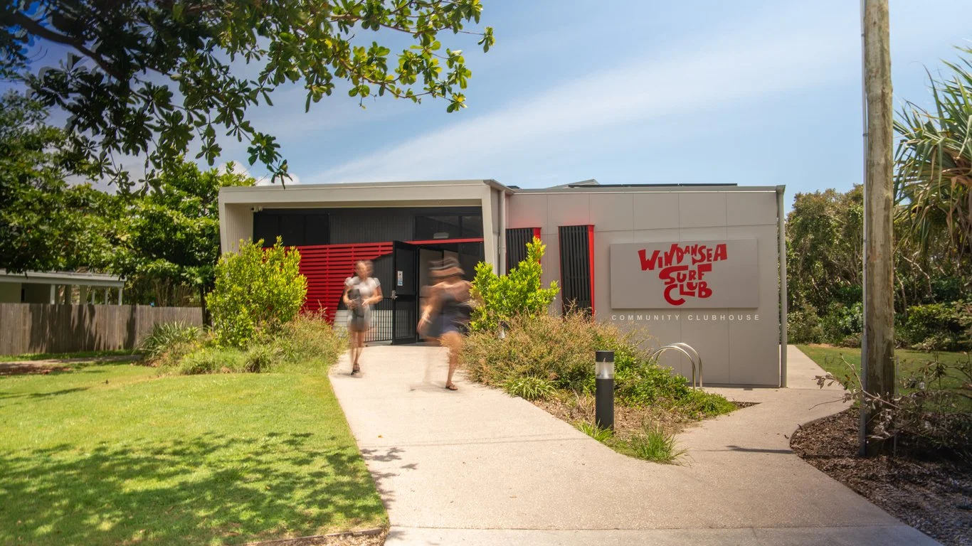 People walking towards a community clubhouse with a sign that reads 'Windsurfer Surf Club' in red letters.