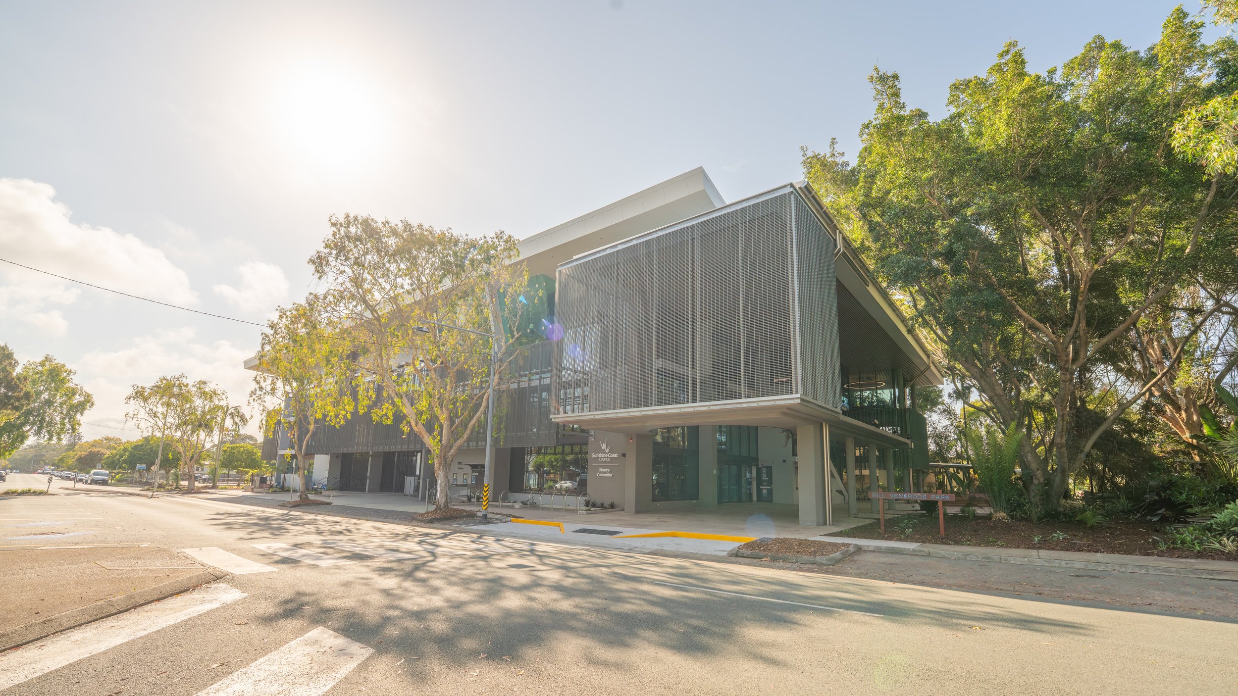 Modern building with metal exterior and trees, bright sunny day, parking lot in foreground.