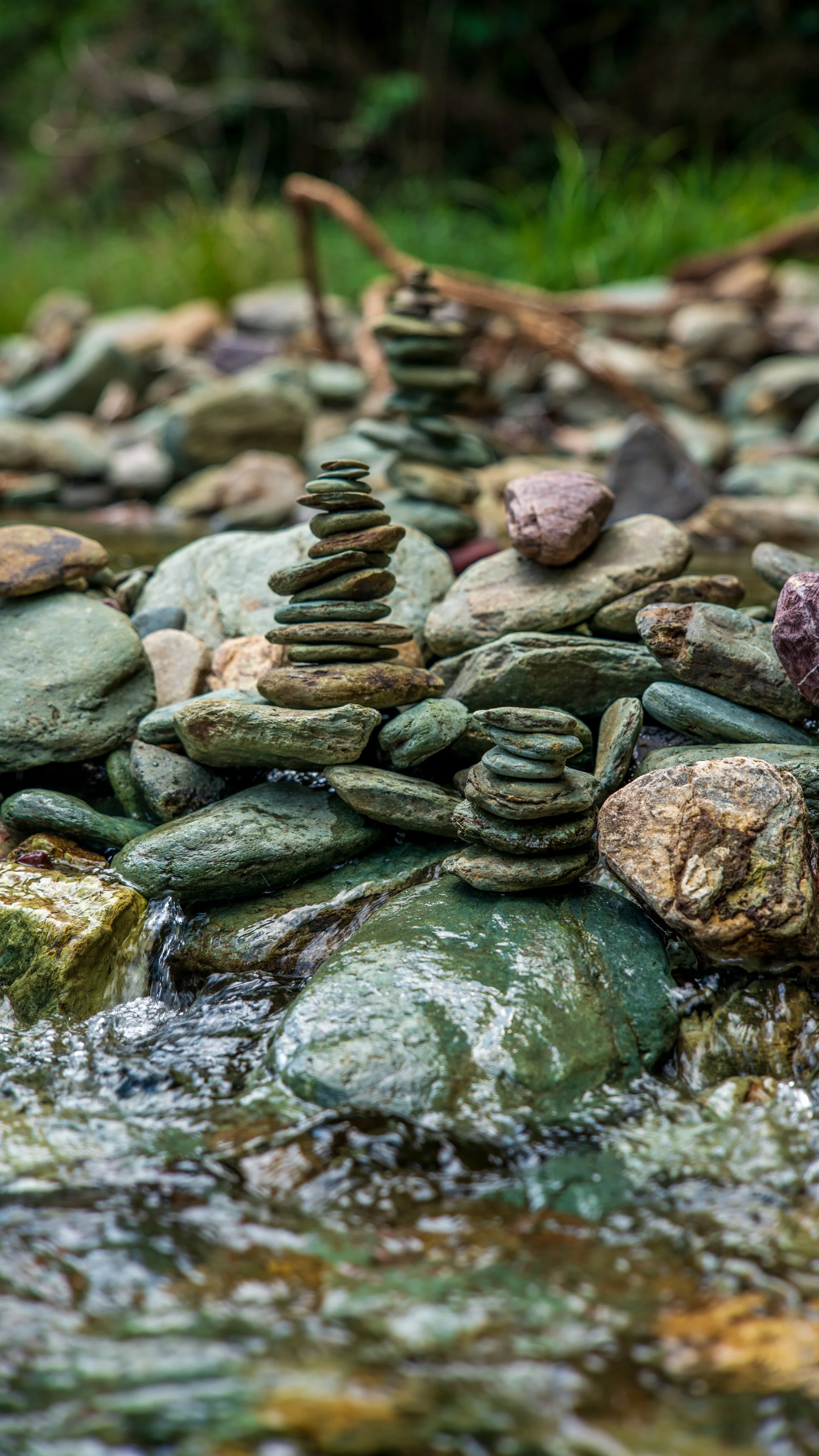 Stacked stones and pebbles on a small stream with greenery in the background.
