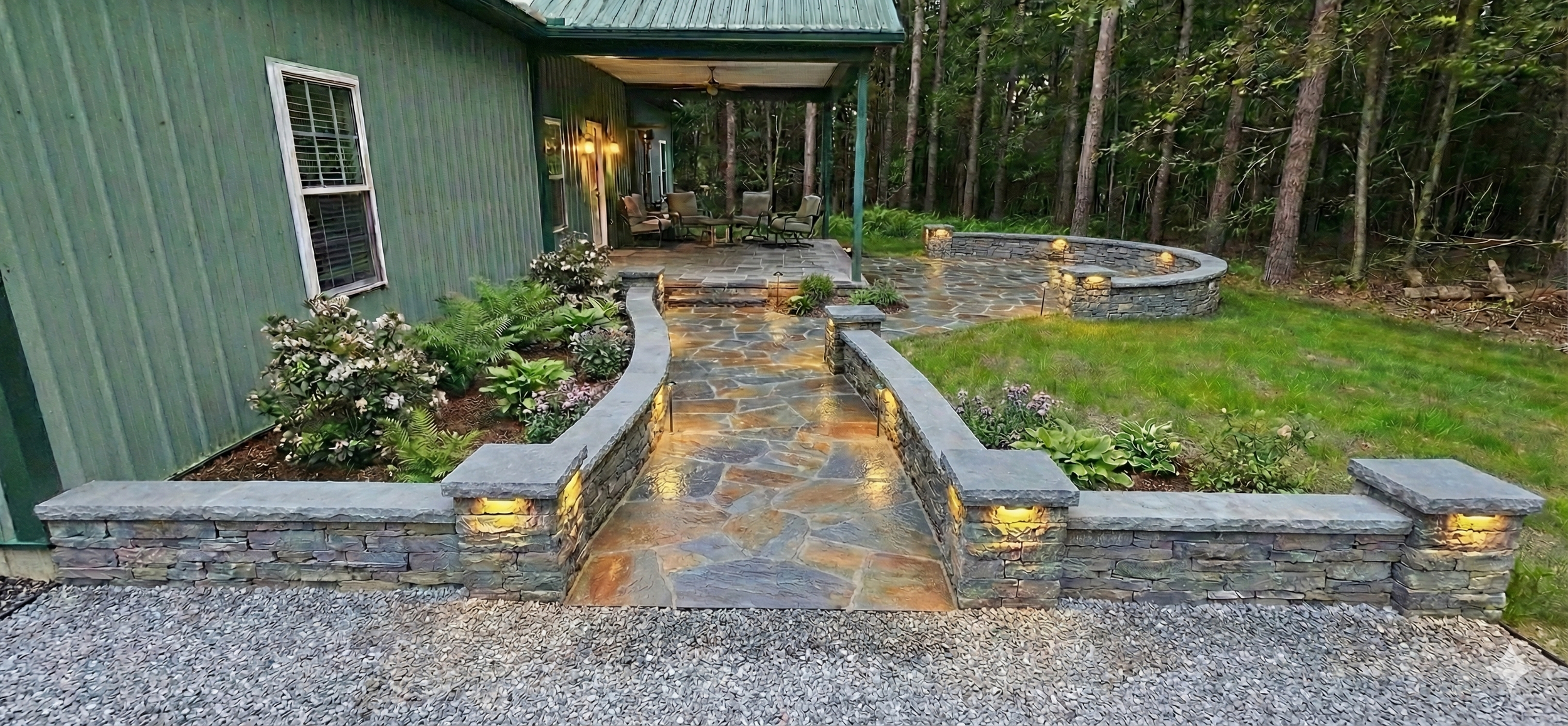 Backyard patio with stone pathway, flower beds, and outdoor seating area, surrounded by trees.
