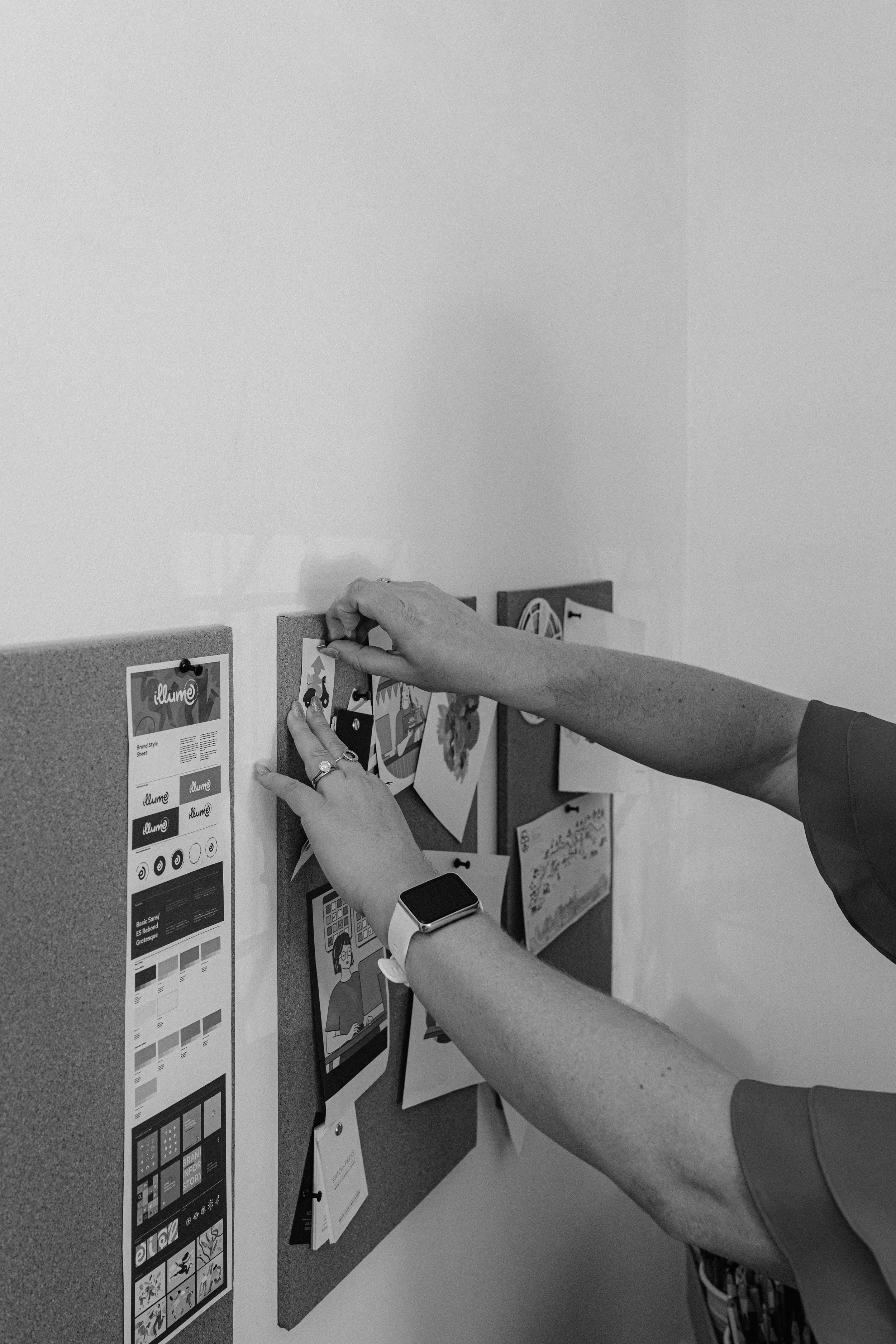 Person pinning notes and images on a corkboard in an office.