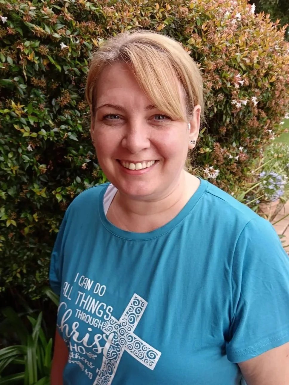 A woman with curly blonde hair smiling outdoors, wearing a blue and white striped shirt.