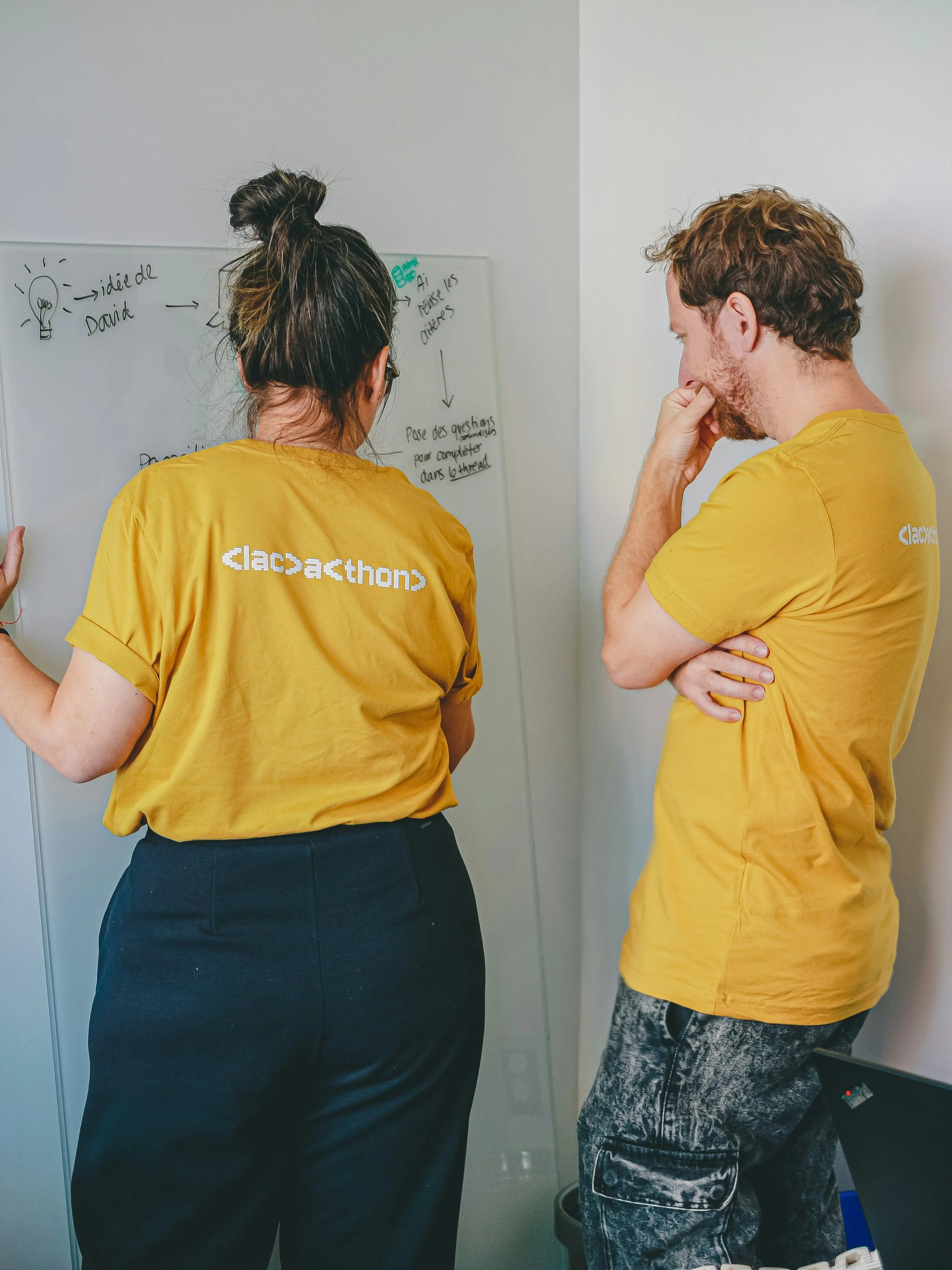 man and woman in yellow t-shirts writing on a whiteboard solving problems