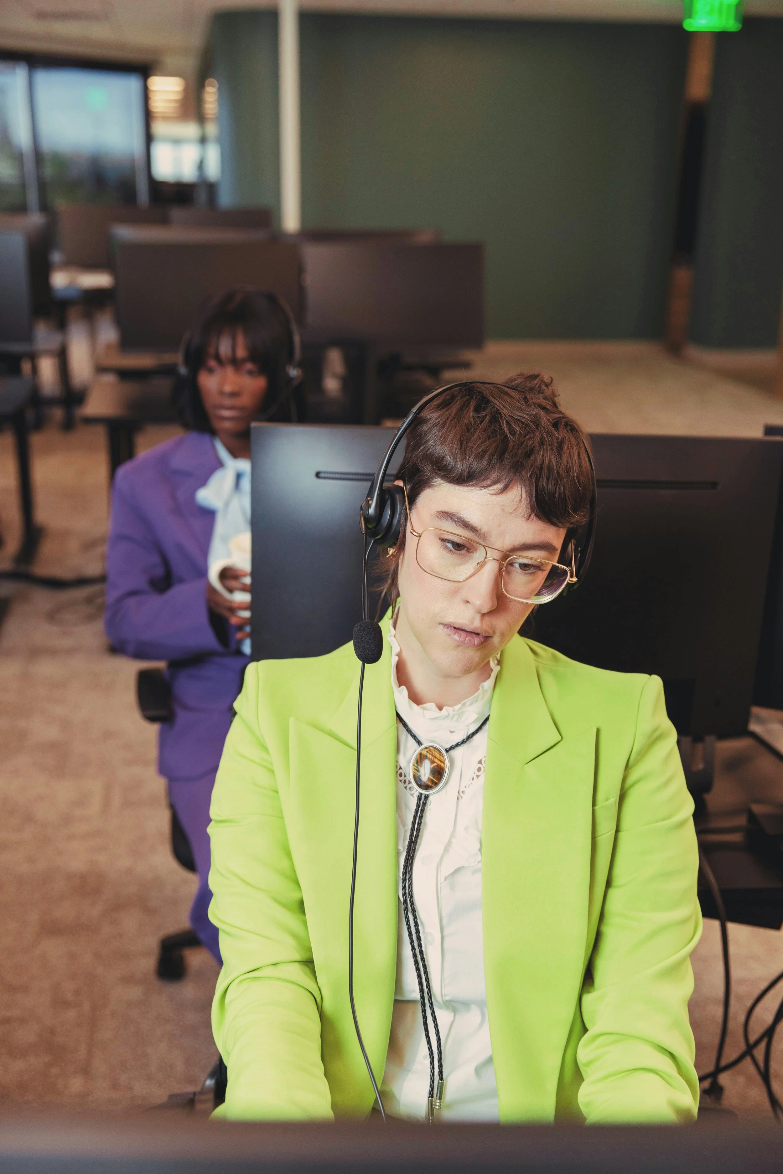 Two bored female call centre workers in bright jackets with headphones