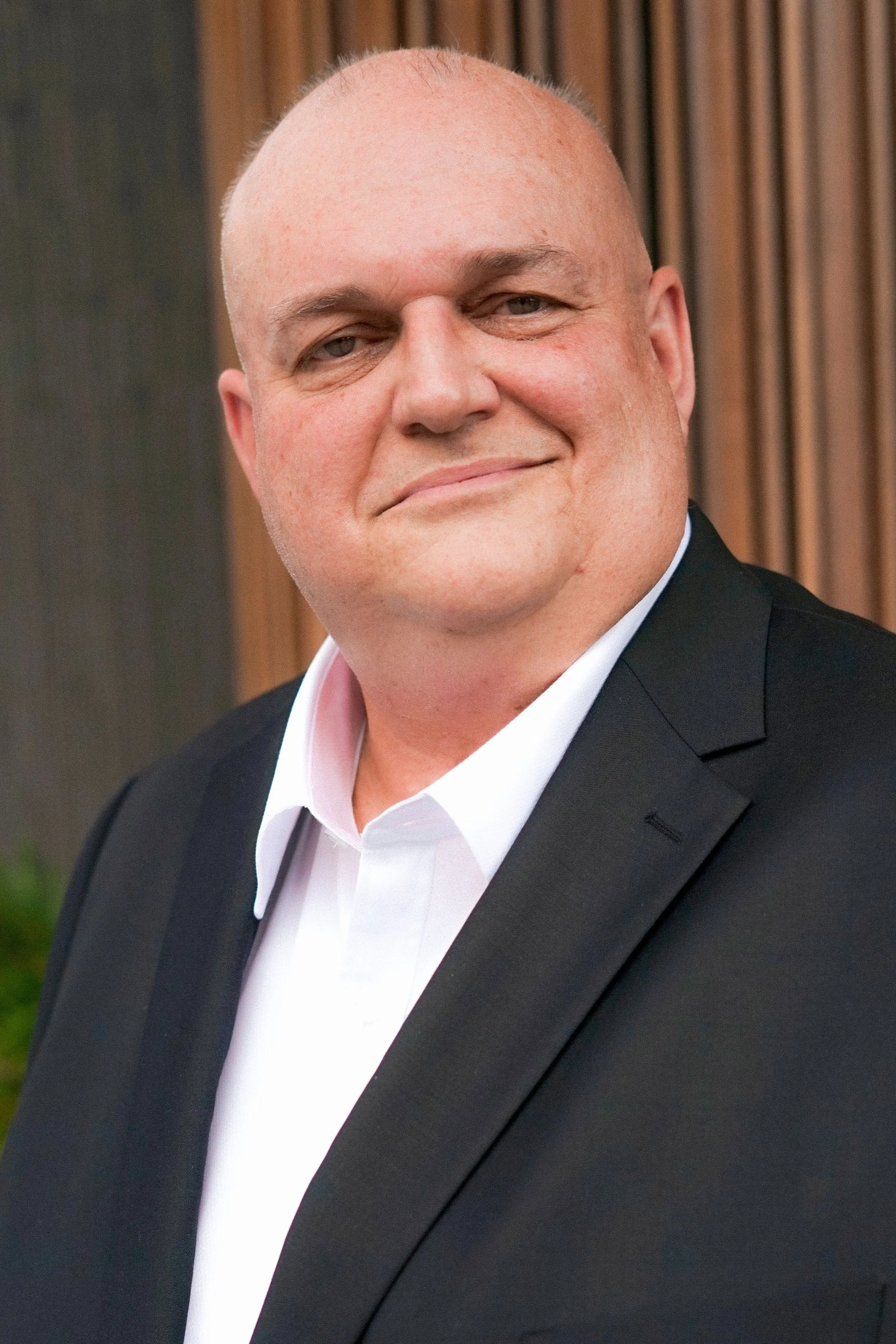 A man in a black suit and white dress shirt smiling at the camera.