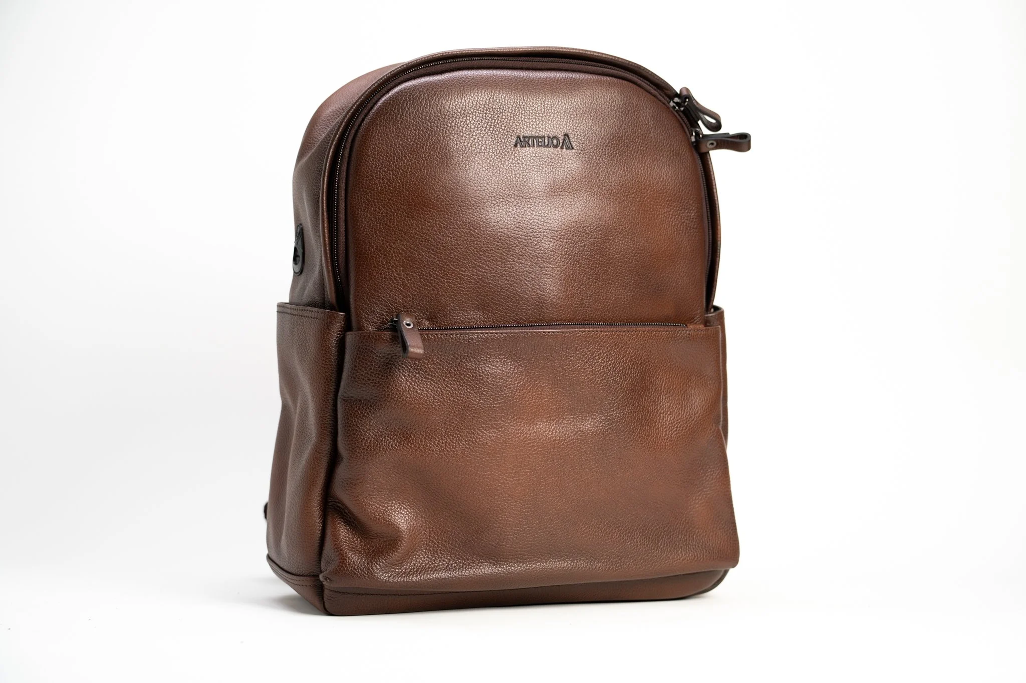 A brown leather backpack with a front zip pocket and a small logo on the top center, photographed against a plain white background.