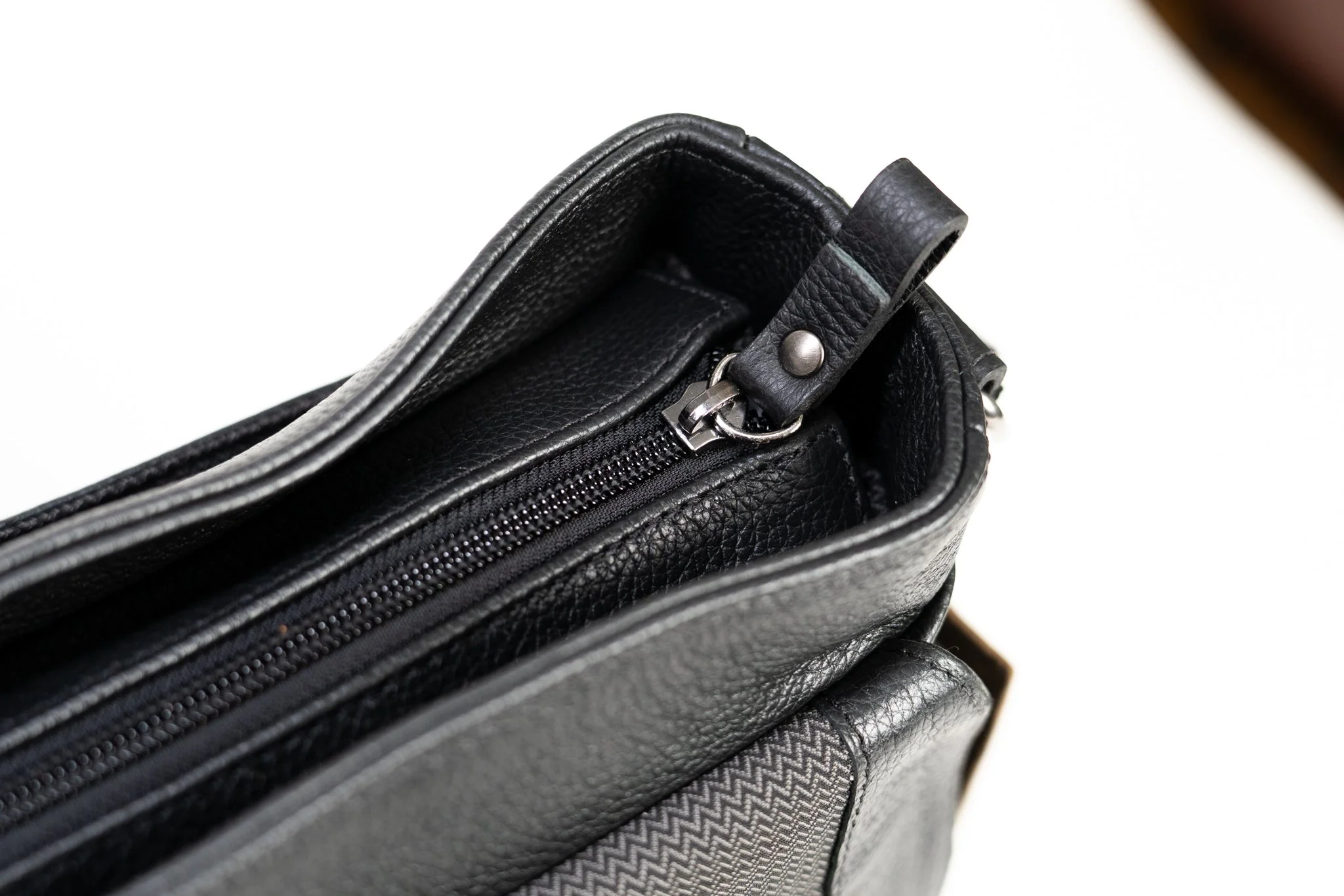 Close-up of a black leather zippered bag with a textured pattern and silver zipper hardware.