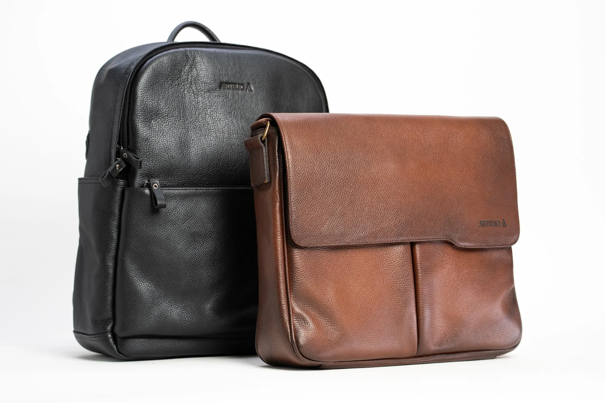 A black leather backpack and a brown leather laptop case placed side by side against a white background.