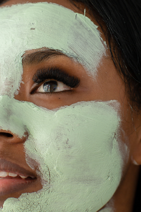 A close-up of a woman with green face mask smeared across her face, focusing on her eye and part of her lips.