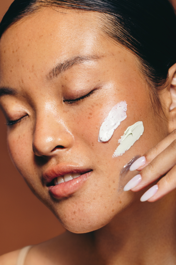 A woman with tan skin and freckles applying skincare cream to her face.