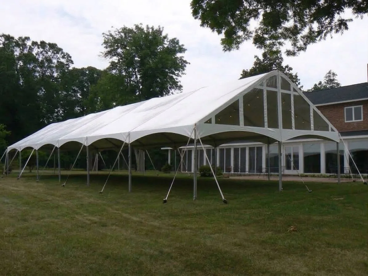 A large frame tent with clear gable ends in a backyard for a wedding