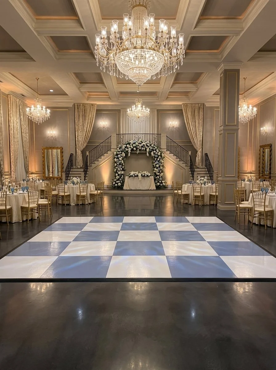 Wide shot of a 15x15 slate blue and white checkered dance floor panel from ATL Dance Floors installed in a fully draped wedding barn venue in Atlanta, Georgia. The glossy surface shows reflections from a central crystal chandelier, surrounded by banq