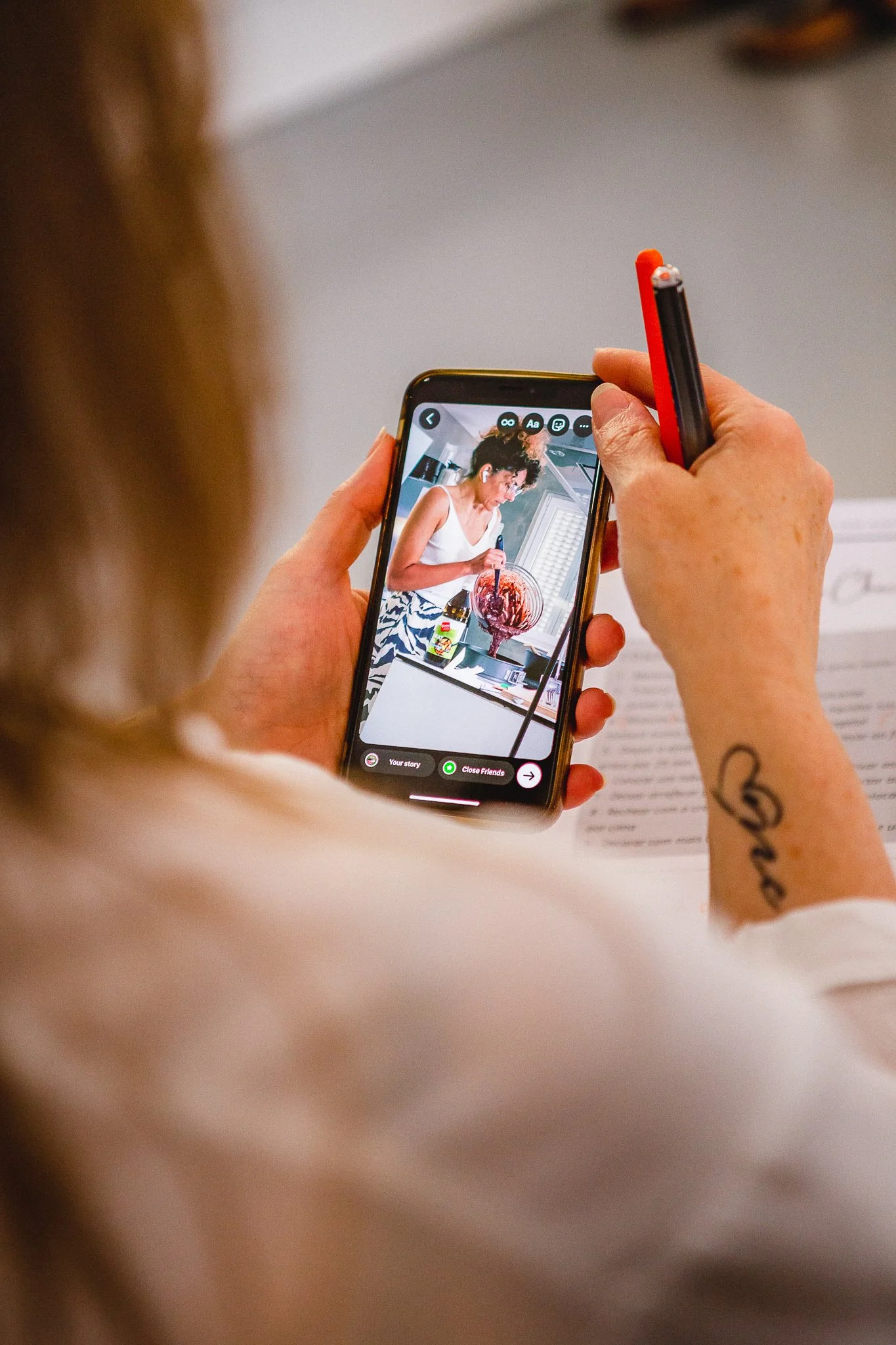 Pessoa segurando um smartphone tirando uma foto de uma mulher que está cozinhando na cozinha.