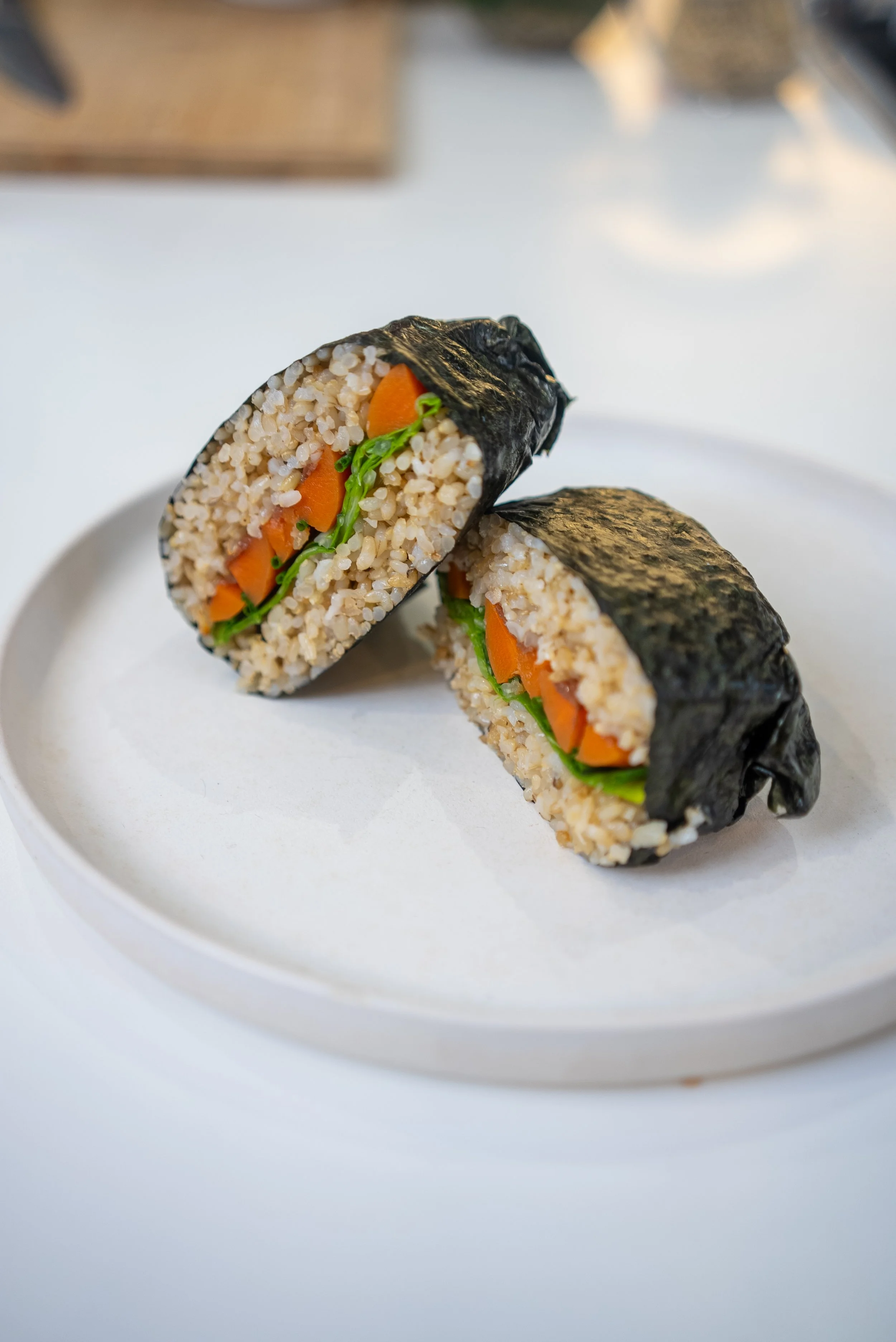 Dois kimbaps cortados ao meio, mostrando arroz, cenoura, alface e nori, em um prato branco.