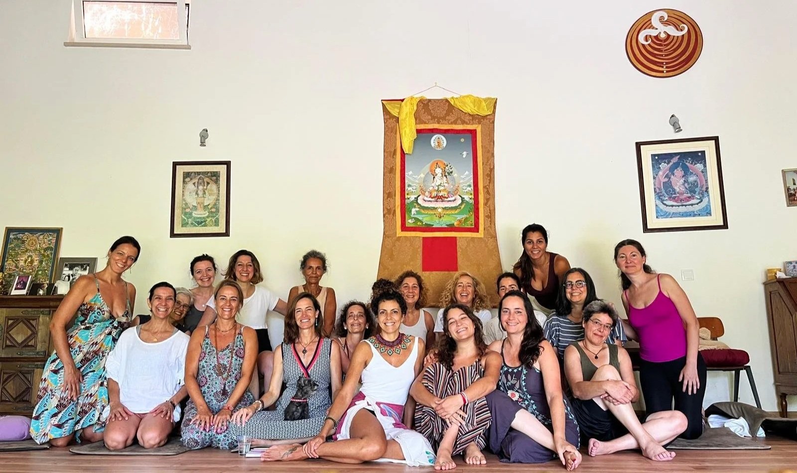 Grupo de mulheres posando para uma foto em um ambiente interno, decorado com imagens religiosas na parede, uma delas dança e outras sorriem.