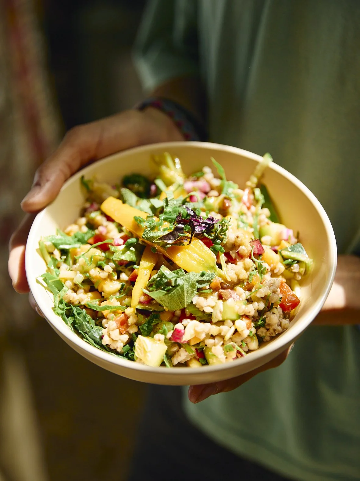 Pessoa segurando uma tigela com salada colorida, contendo verduras, legumes e grãos.
