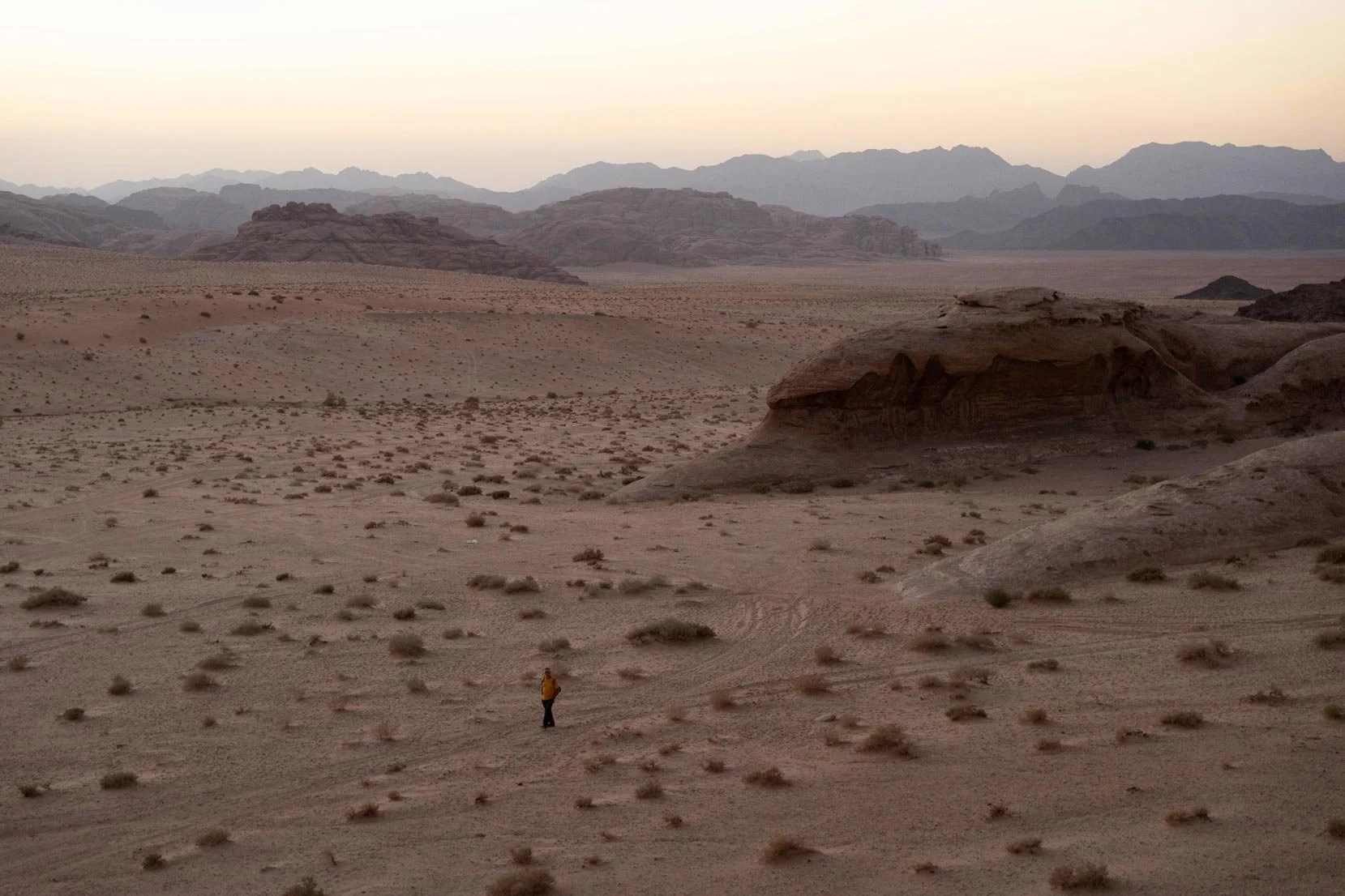 A person in a yellow jacket standing in the Wadi Rum dessert in Jordan.