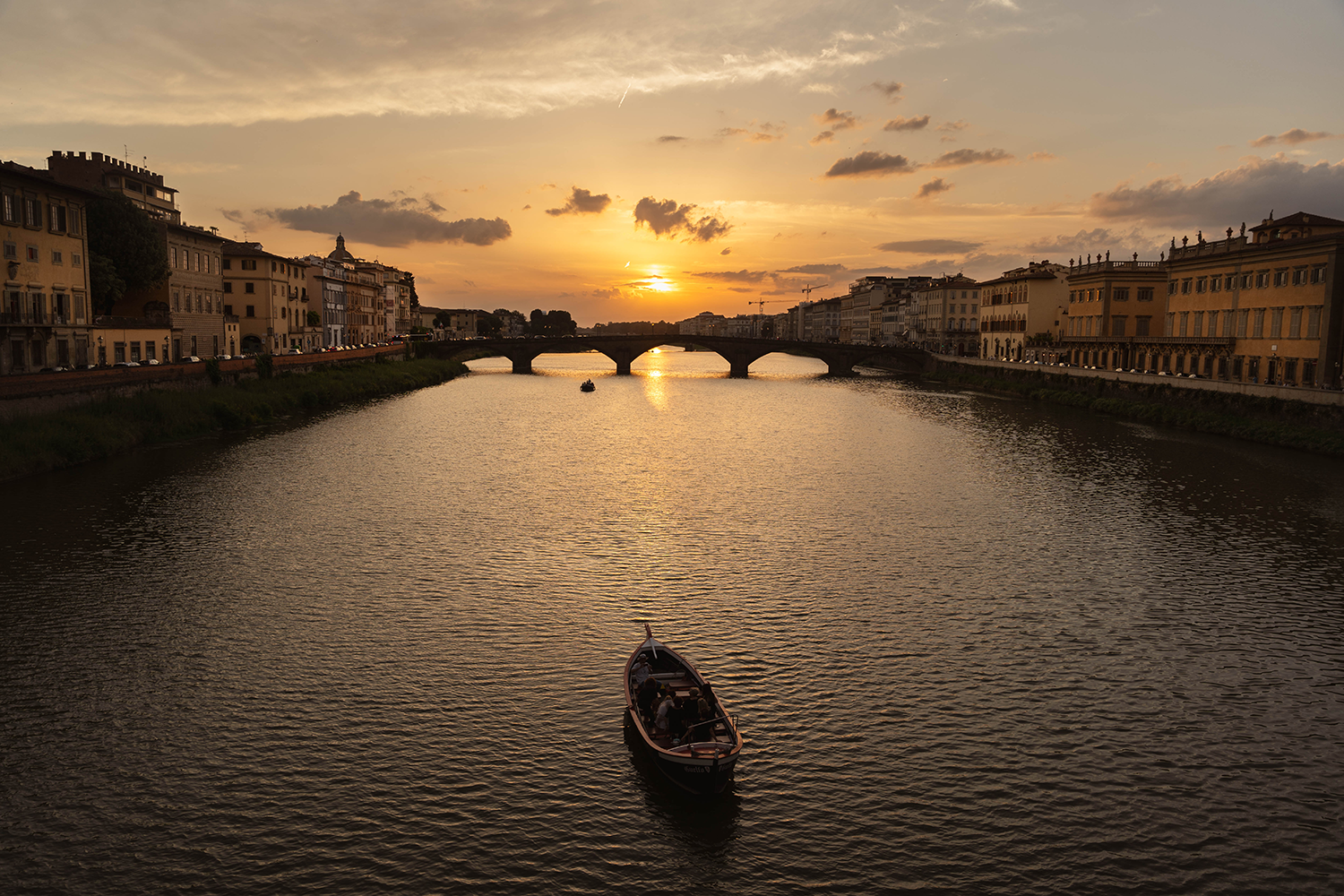 Sunset over a river with a boat in the foreground in Florence, Italy