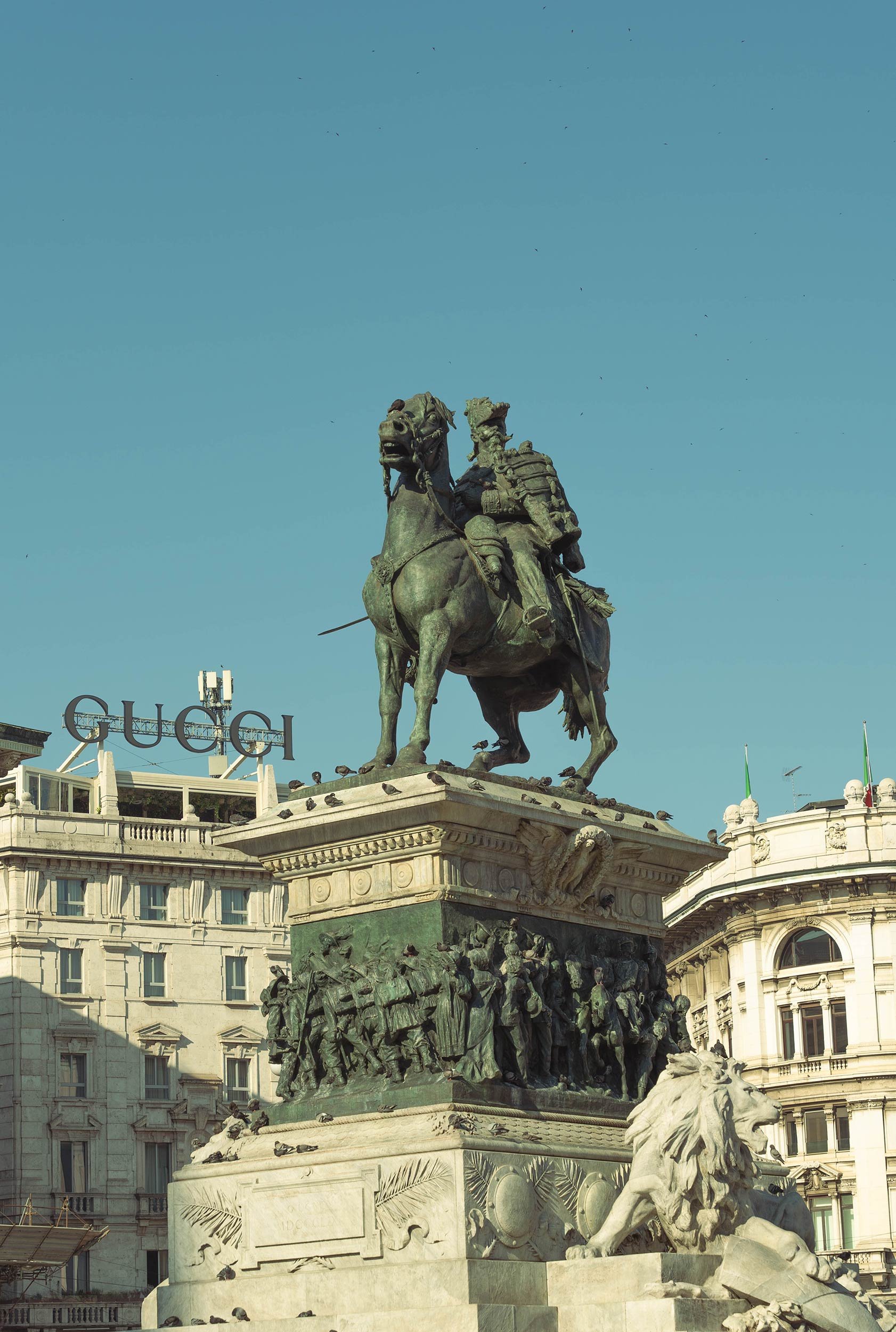 Monument to Vittorio Emanuele II statue in front of Duomo di Milano with Gucci building in background.
