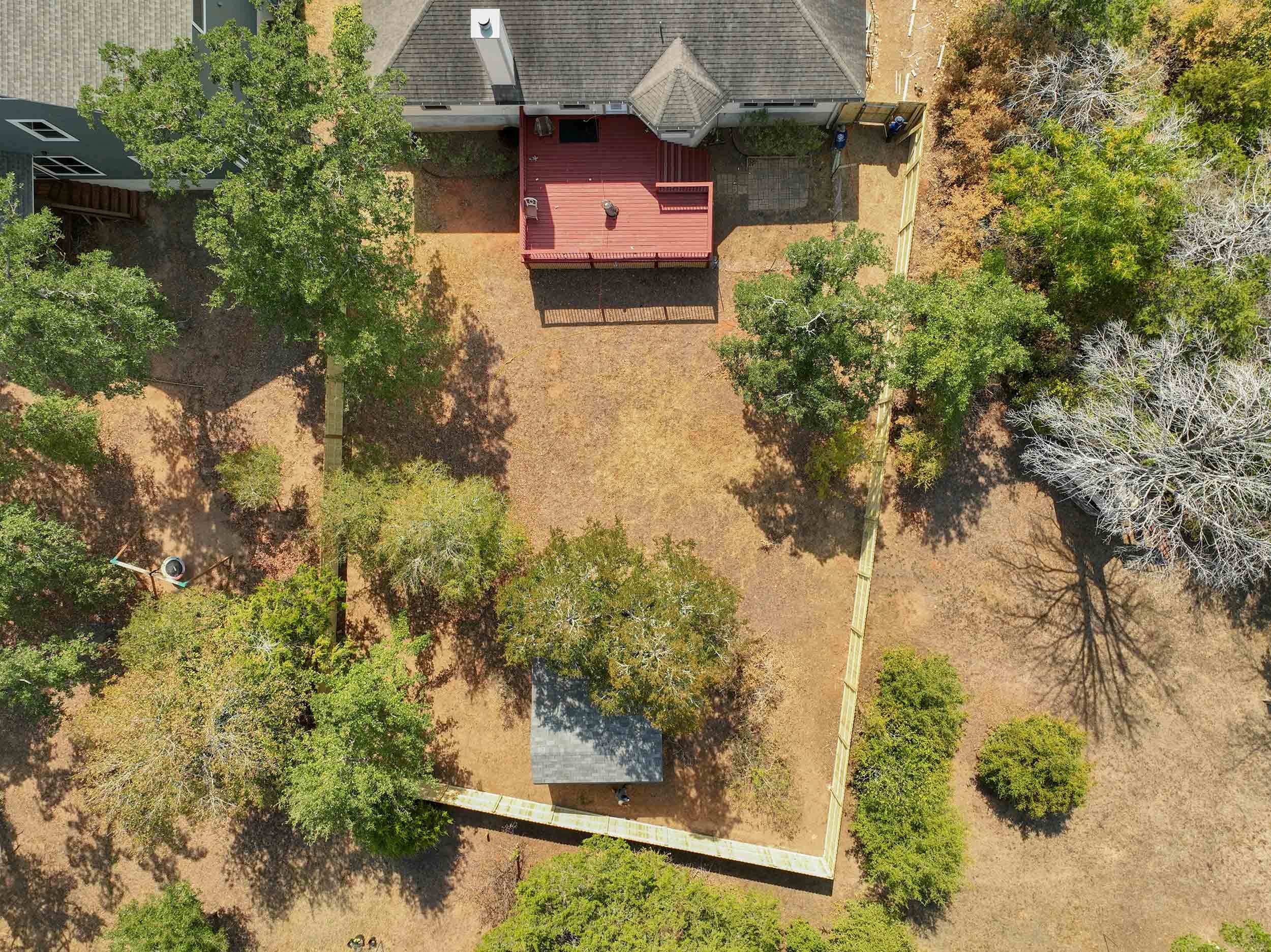 Aerial view of a backyard with trees, a wooden deck, and a small shed, surrounded by a wooden fence.