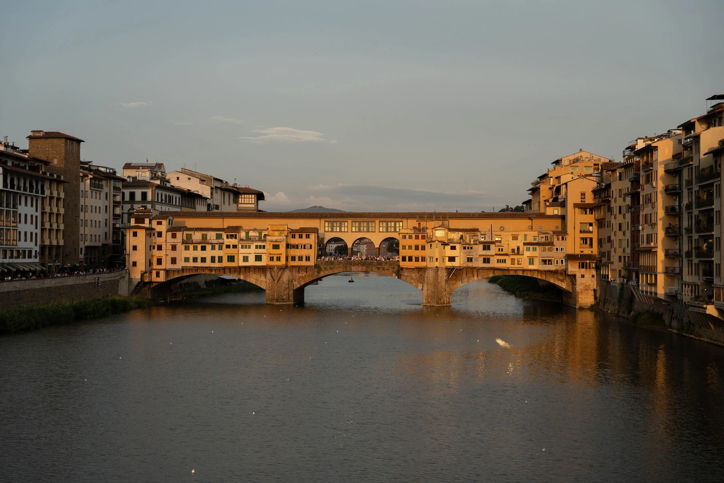 Sunset view of Ponte Vecchio, a medieval stone bridge with shops, over the Arno River in Florence, Italy.