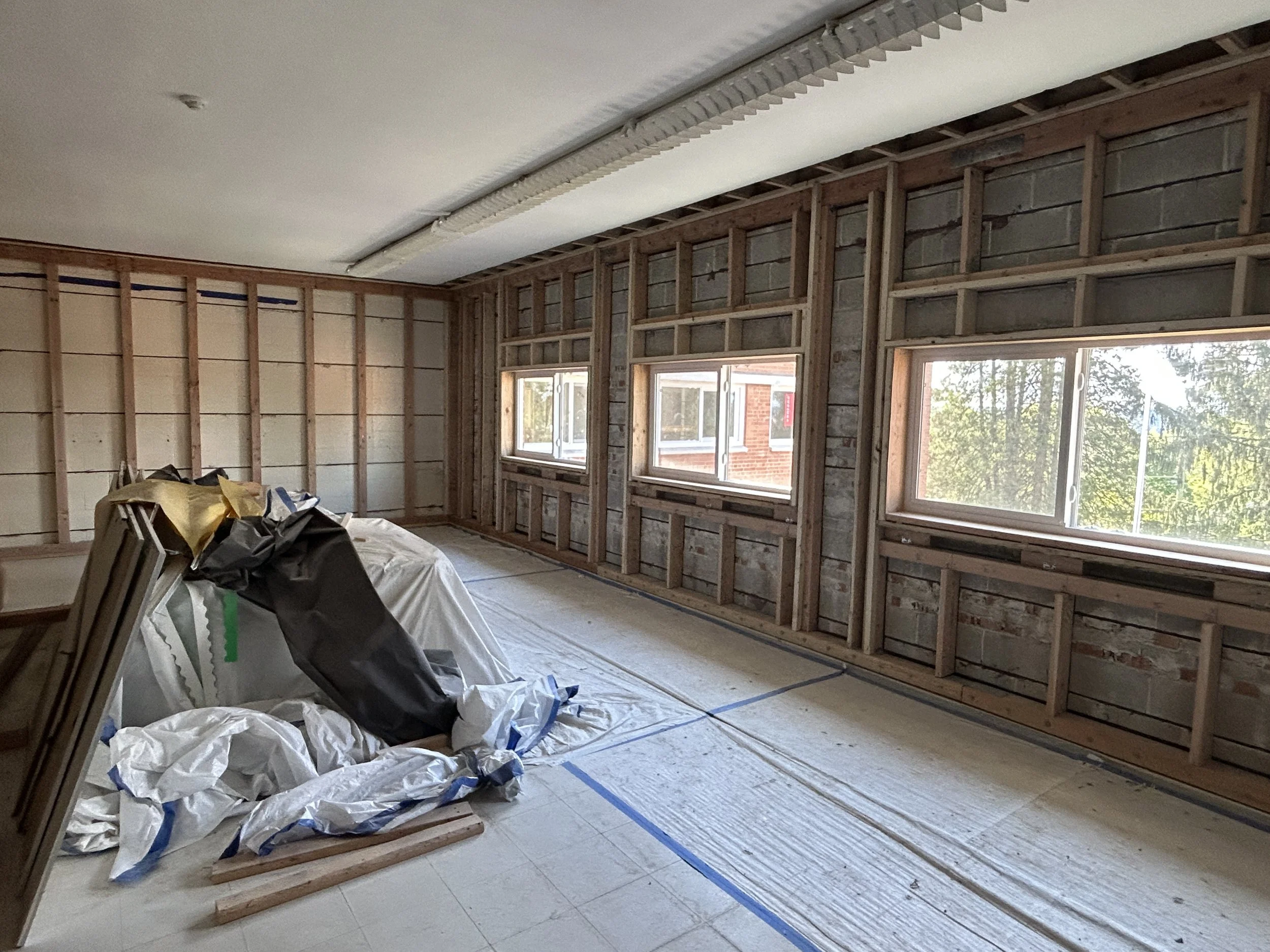 Classroom interior during strip-out with exposed studs, masonry, and new window openings