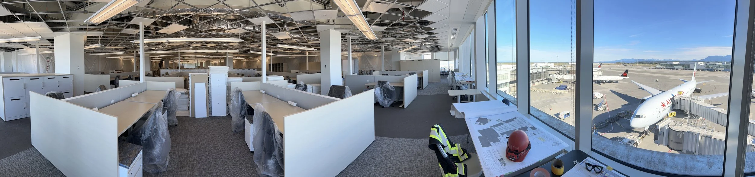Panoramic view of airport terminal office fit-out with open ceiling and workstations overlooking airside gates