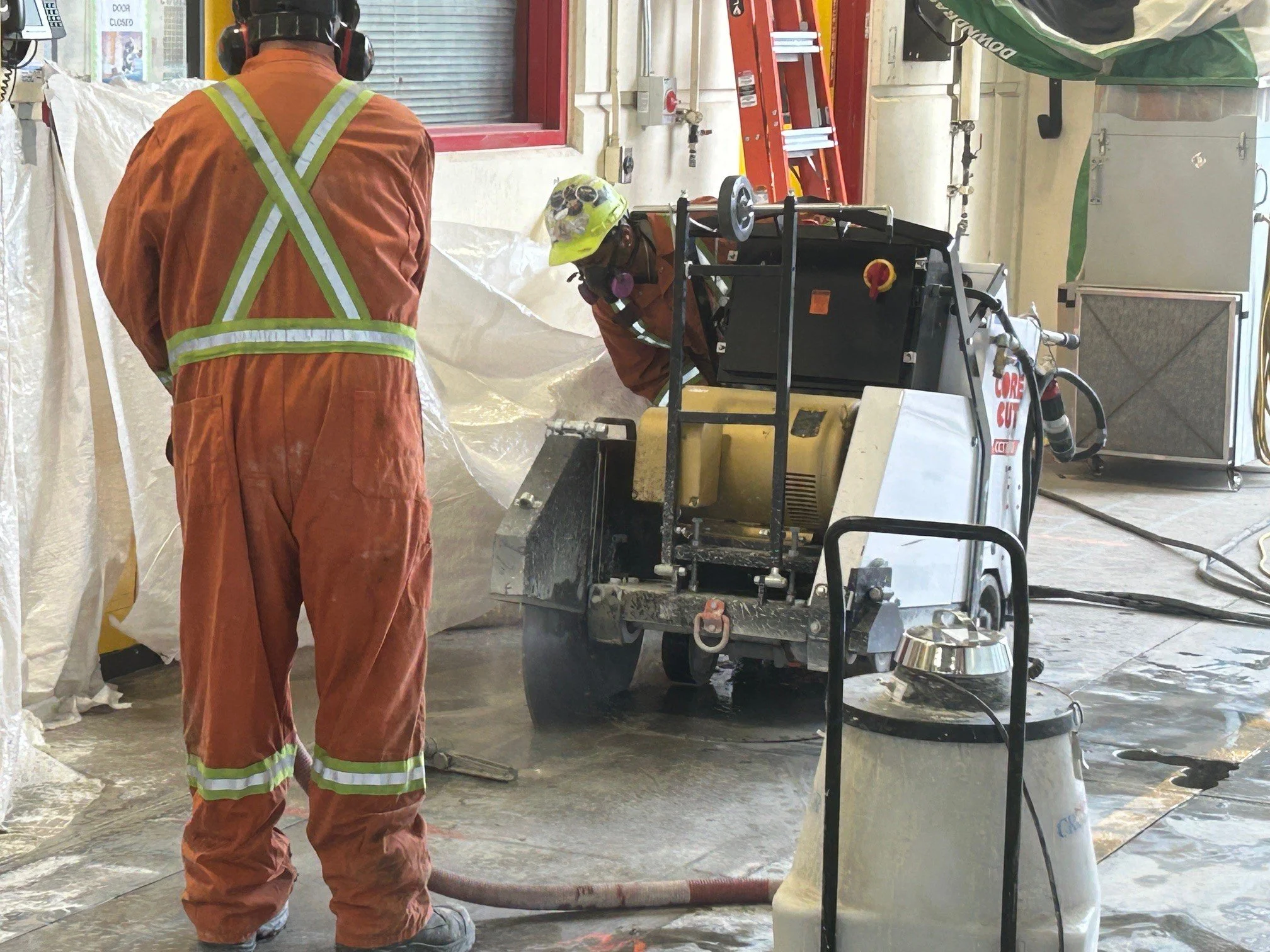 Technicians cutting a concrete slab inside a transit maintenance bay with dust control and PPE