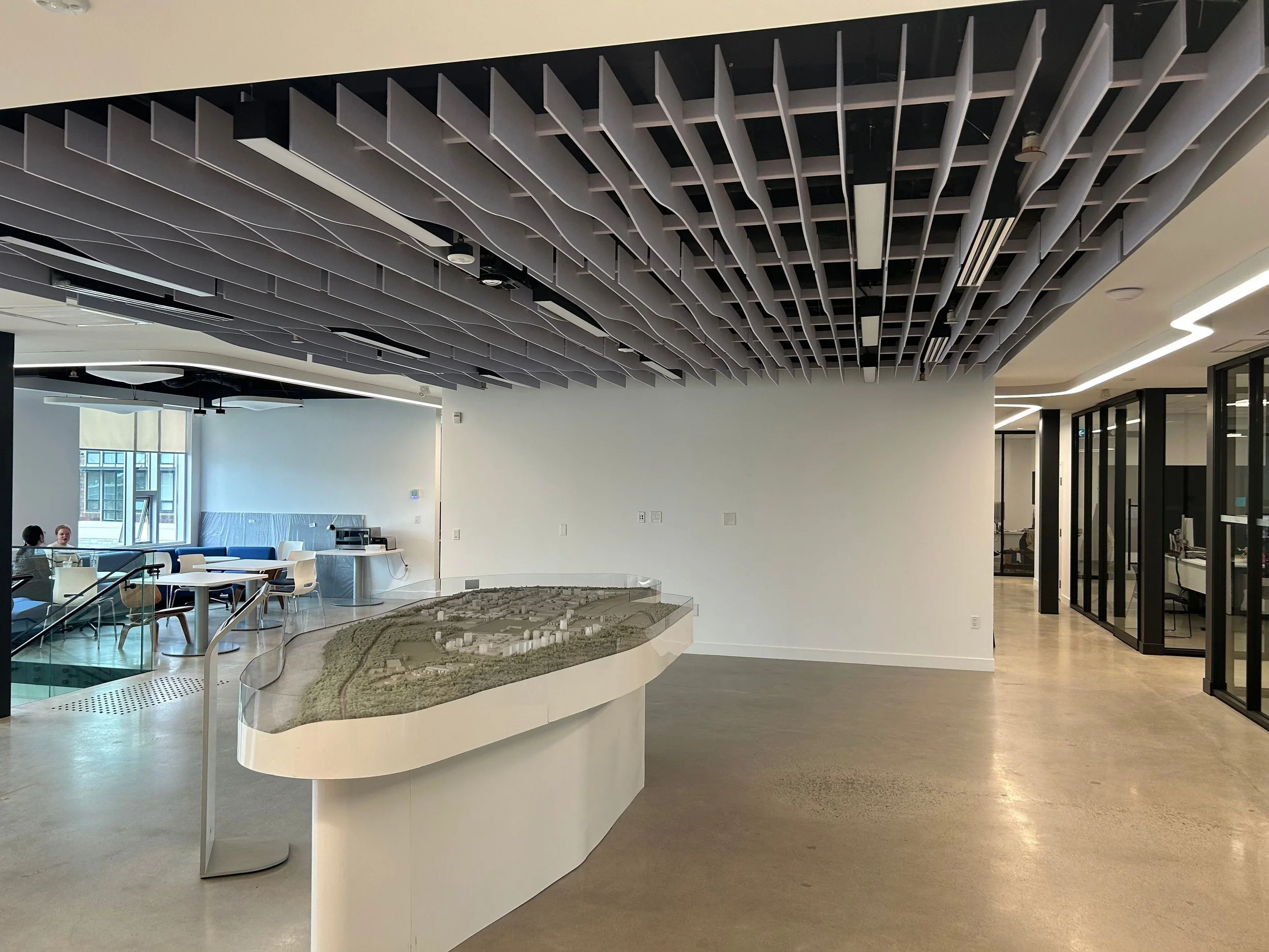 Office lobby with architectural site model, acoustic ceiling baffles, polished concrete floor, and meeting area