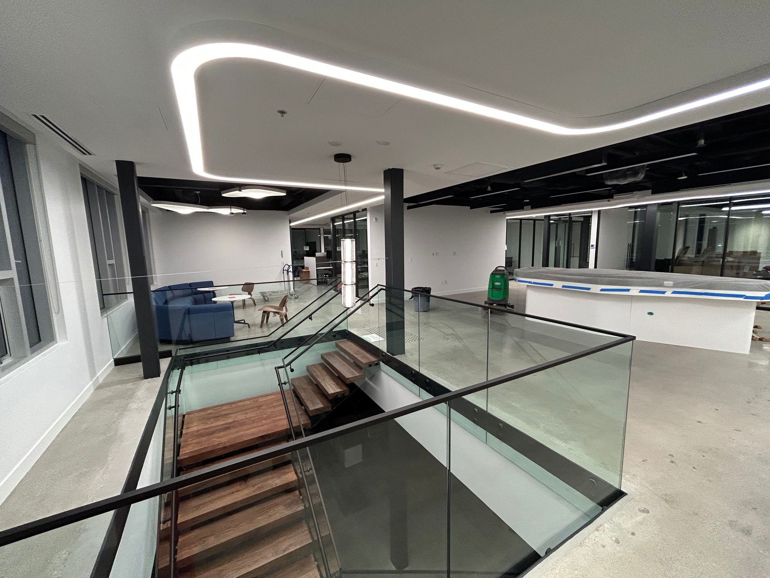 Interior office renovation featuring wood feature stair with glass guardrails and open-plan workspace