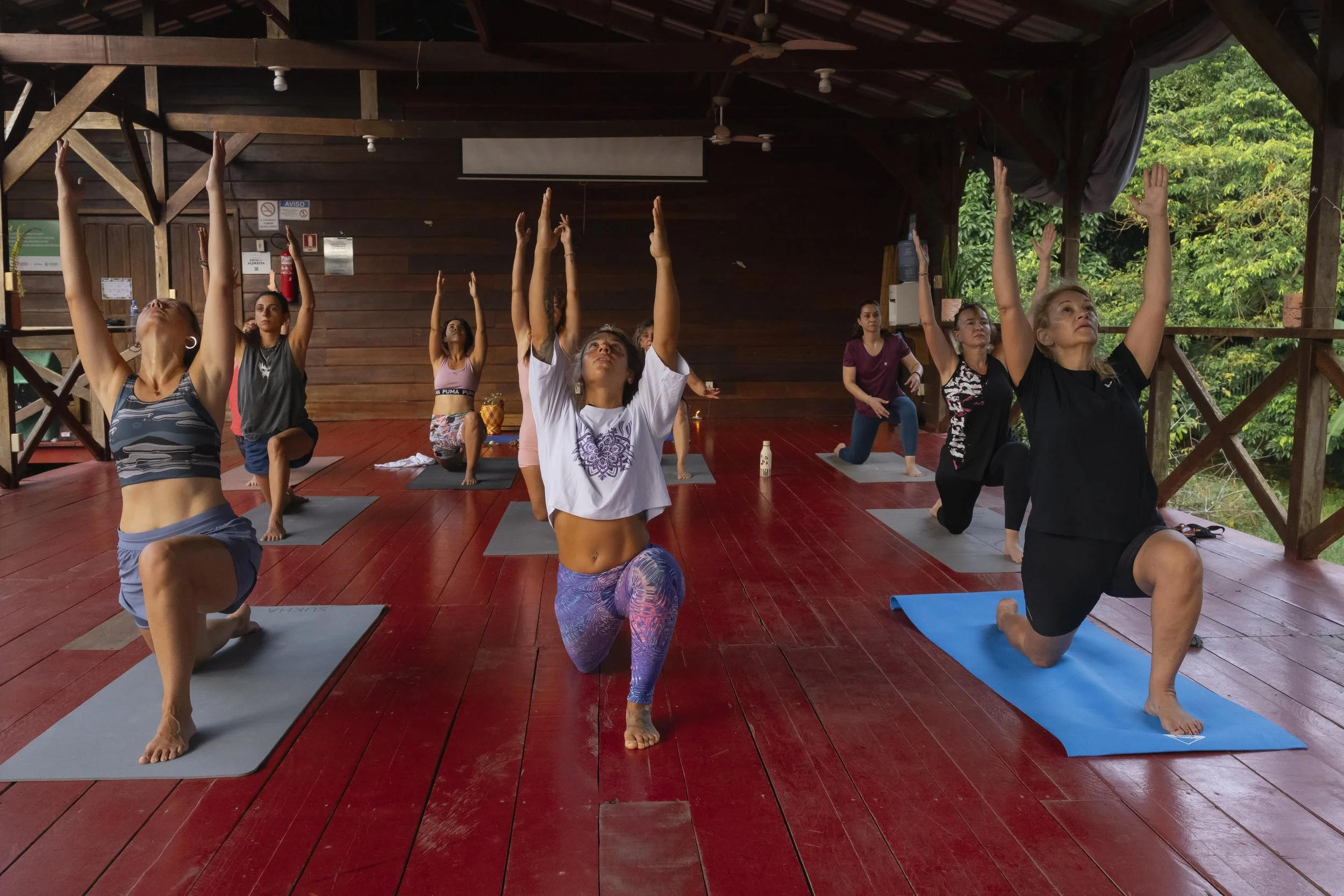 Grupo de personas participando en una clase de meditación o yoga en un espacio abierto con plantas y decoraciones artesanales.