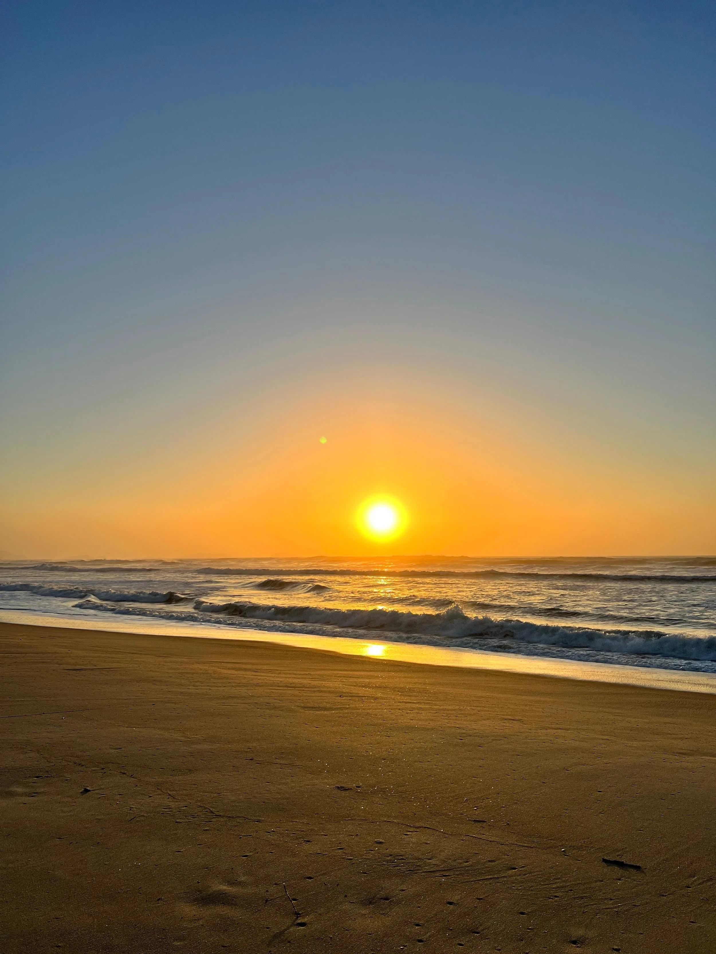 Atardecer en la playa con sol brillante en el horizonte y olas que llegan a la orilla de arena.