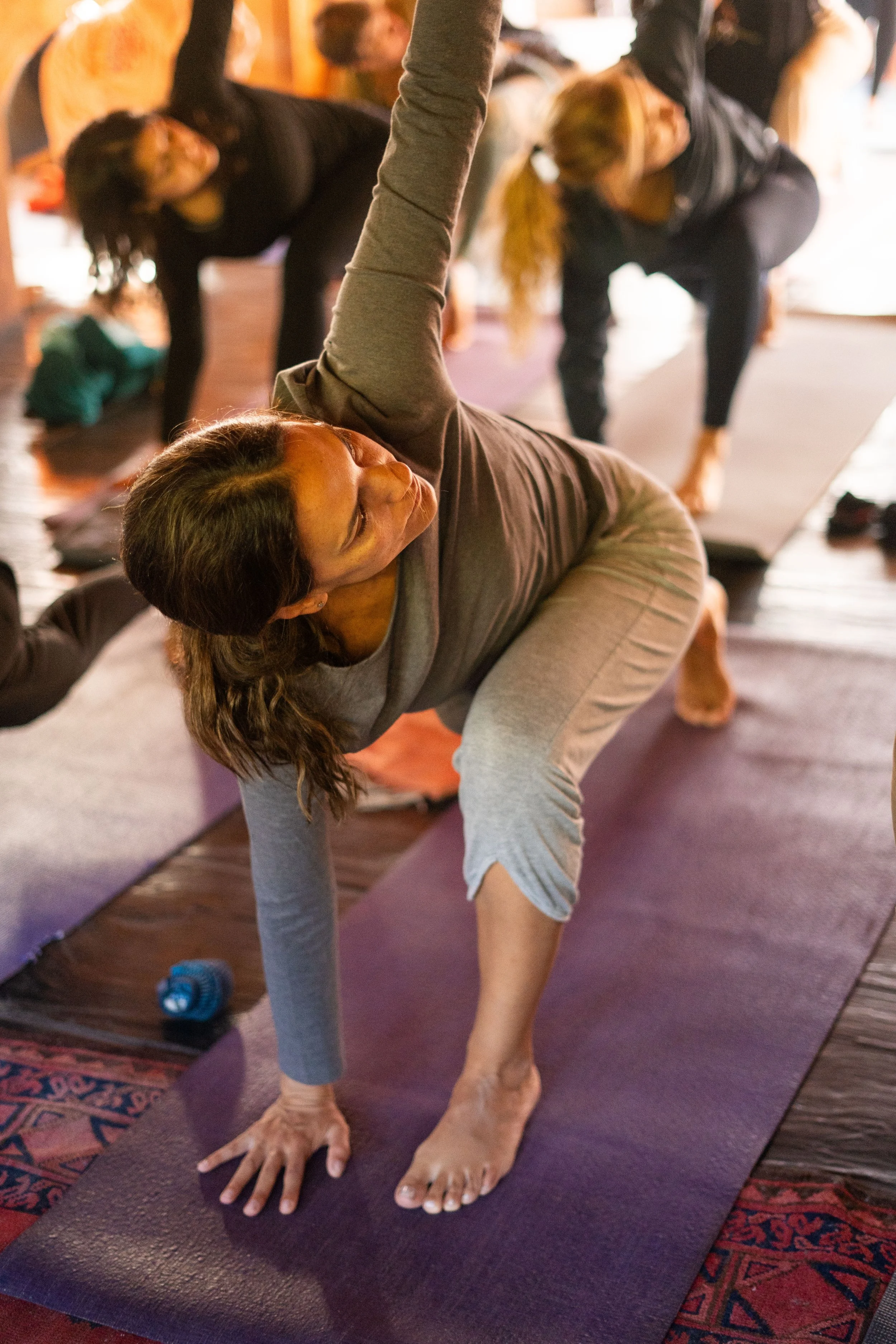 Grupo de personas practicando yoga en una terraza de madera junto a una piscina, con vista a montañas y árboles verdes.