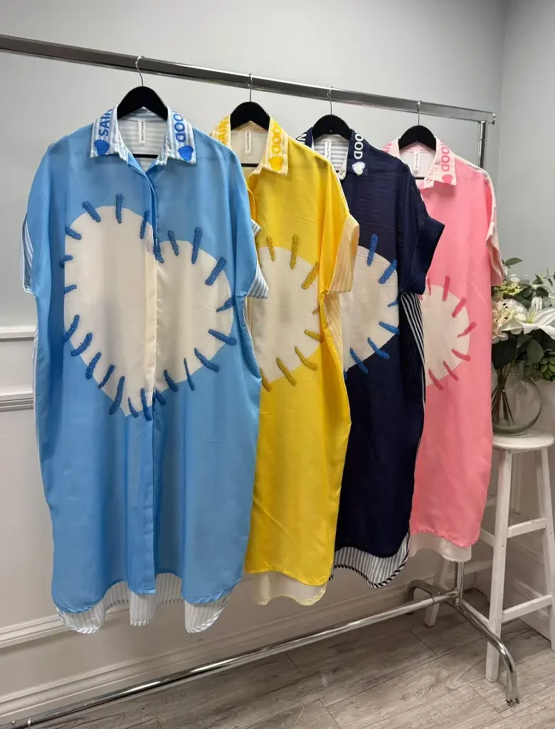 Four colorful oversized shirts hanging on a clothing rack, each featuring a sun graphic design on the front in different colors: blue, yellow, navy, and pink.
