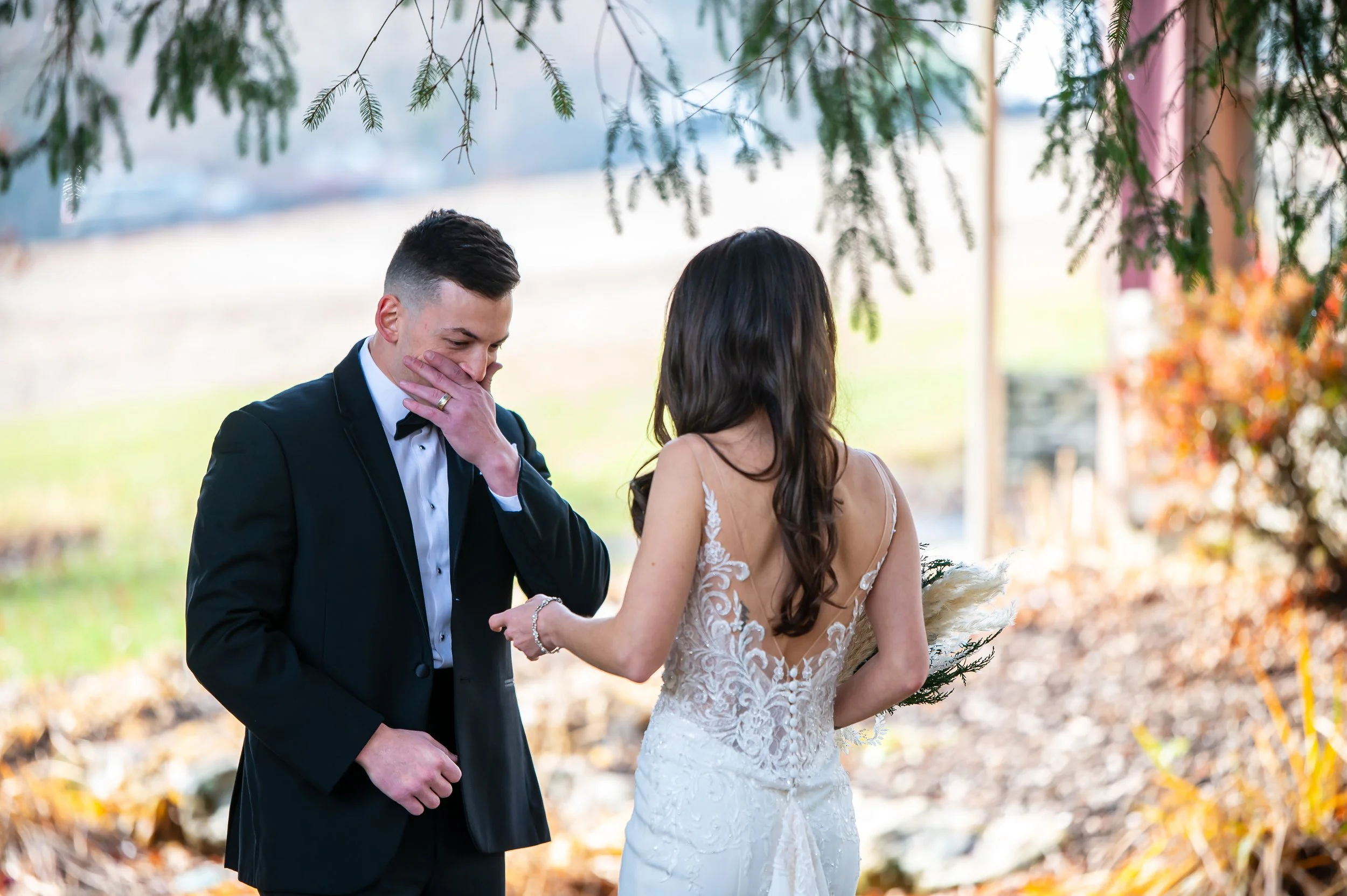 A bride and groom exchanging rings outdoors during their wedding ceremony, with the groom visibly emotional.