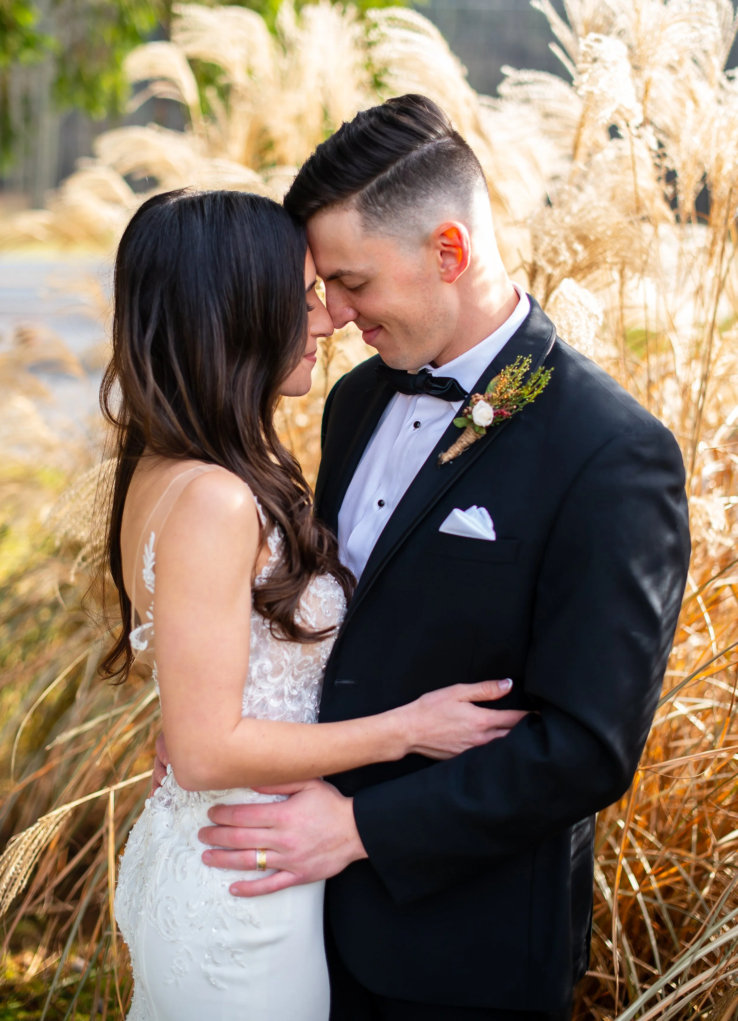 A bride and groom sharing a kiss outdoors surrounded by tall, dry grasses during their wedding photoshoot.
