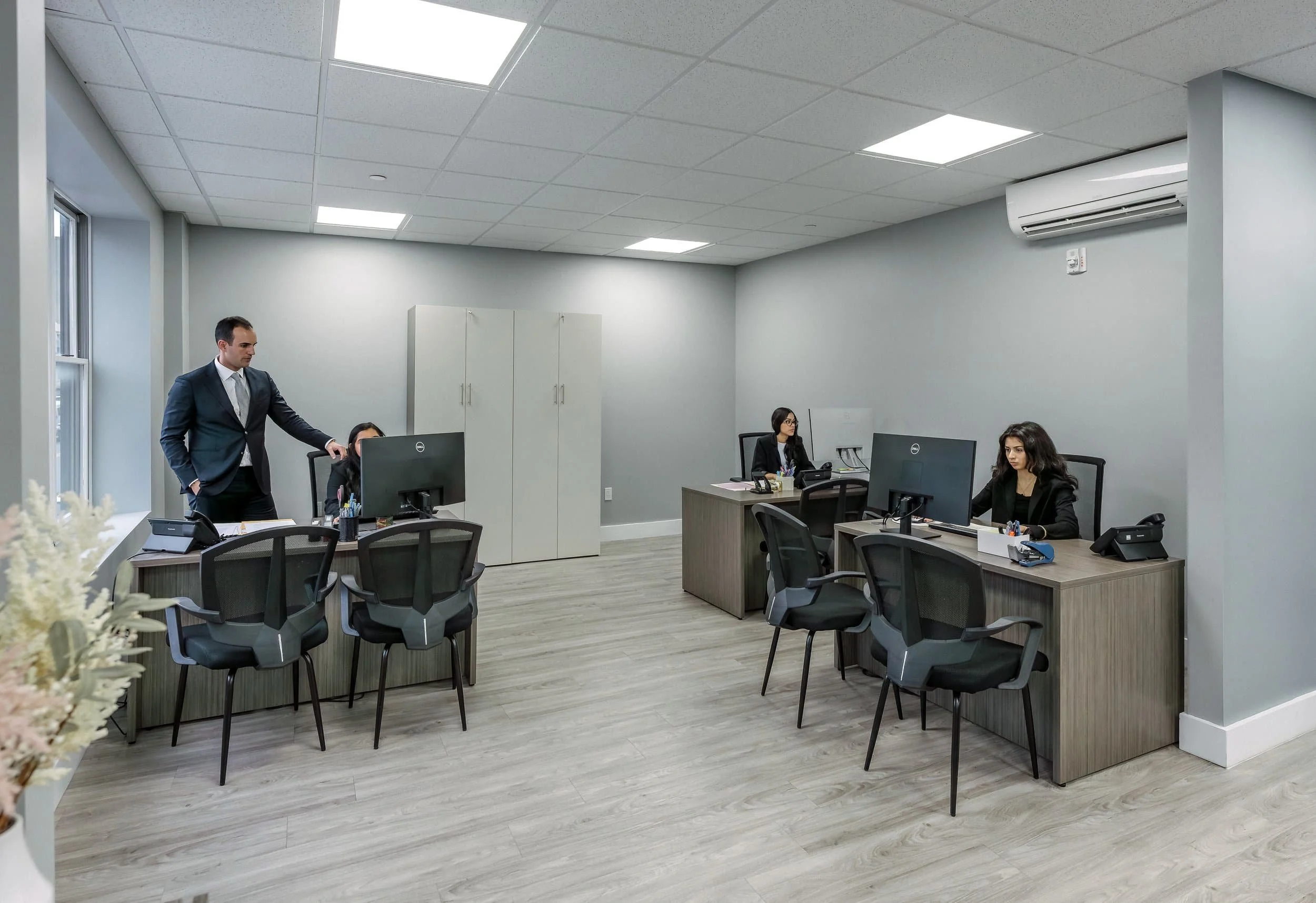 Modern office with three people working at desks with computers and one person standing, all in a bright, minimalist space.