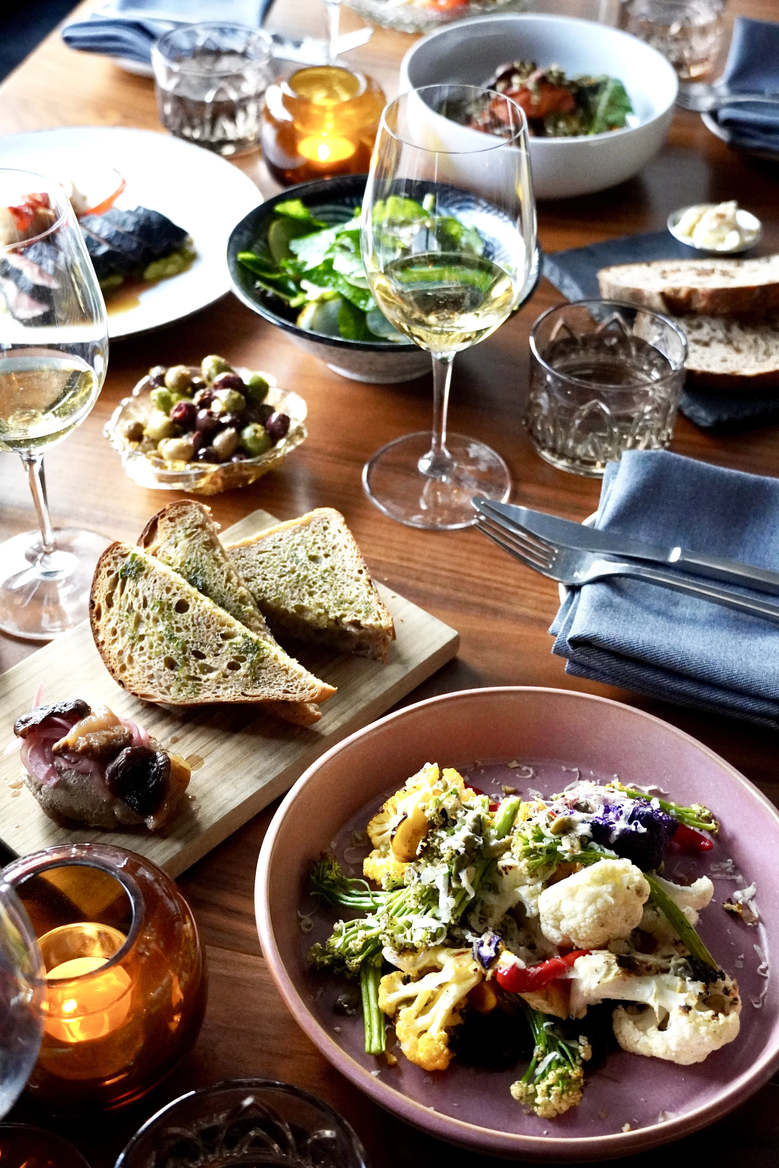Farm-to-table dishes, fresh bread, seasonal vegetables, and natural wine shared across the table at Cork Restaurant in Stowe, Vermont, reflecting communal dining and seasonal cooking.