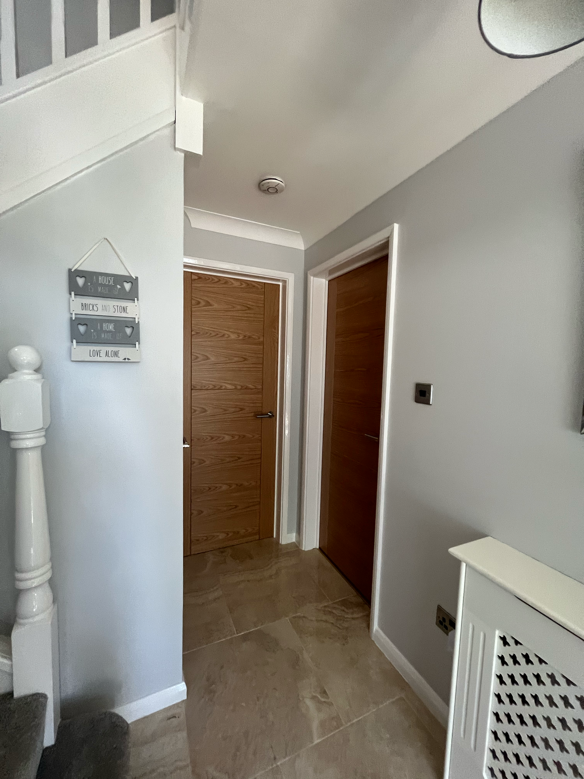 Interior of a house hallway with a staircase, two wooden doors, white walls, and a wall decoration with a motivational quote.
