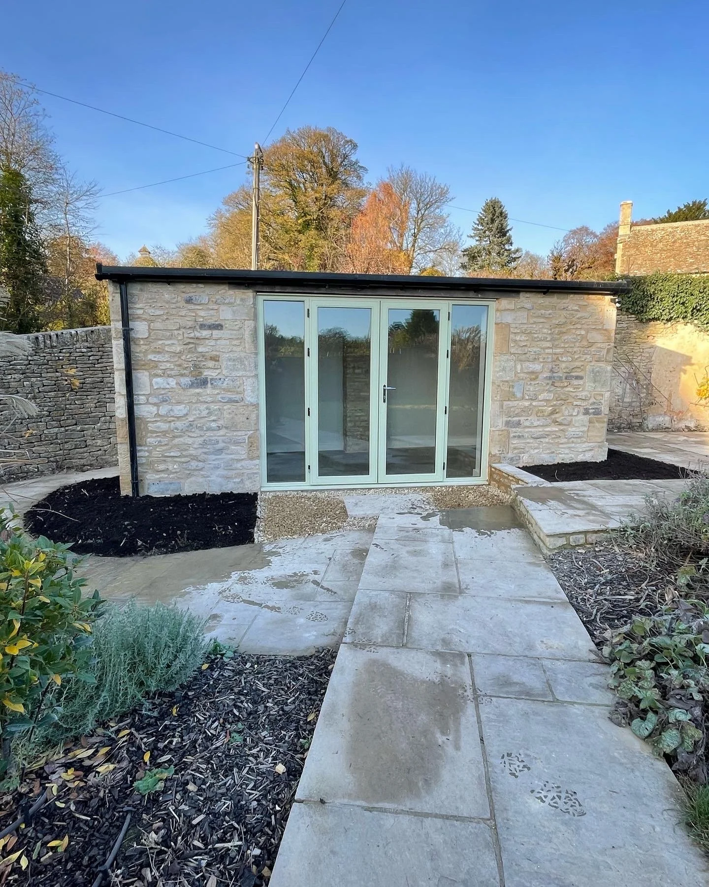 Small stone garden building with glass doors in a landscaped yard