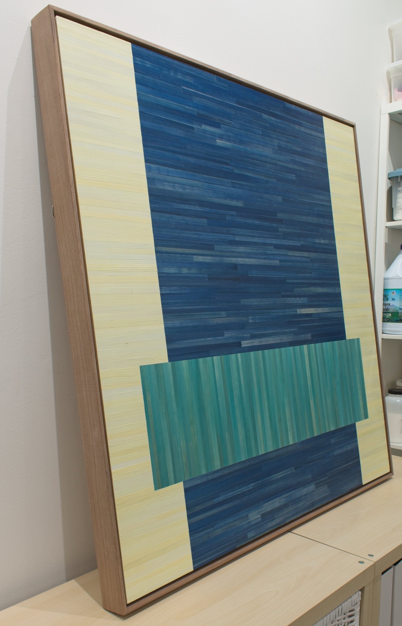 Side view of blue and teal straw marquetry geometric artwork. Float framed in walnut