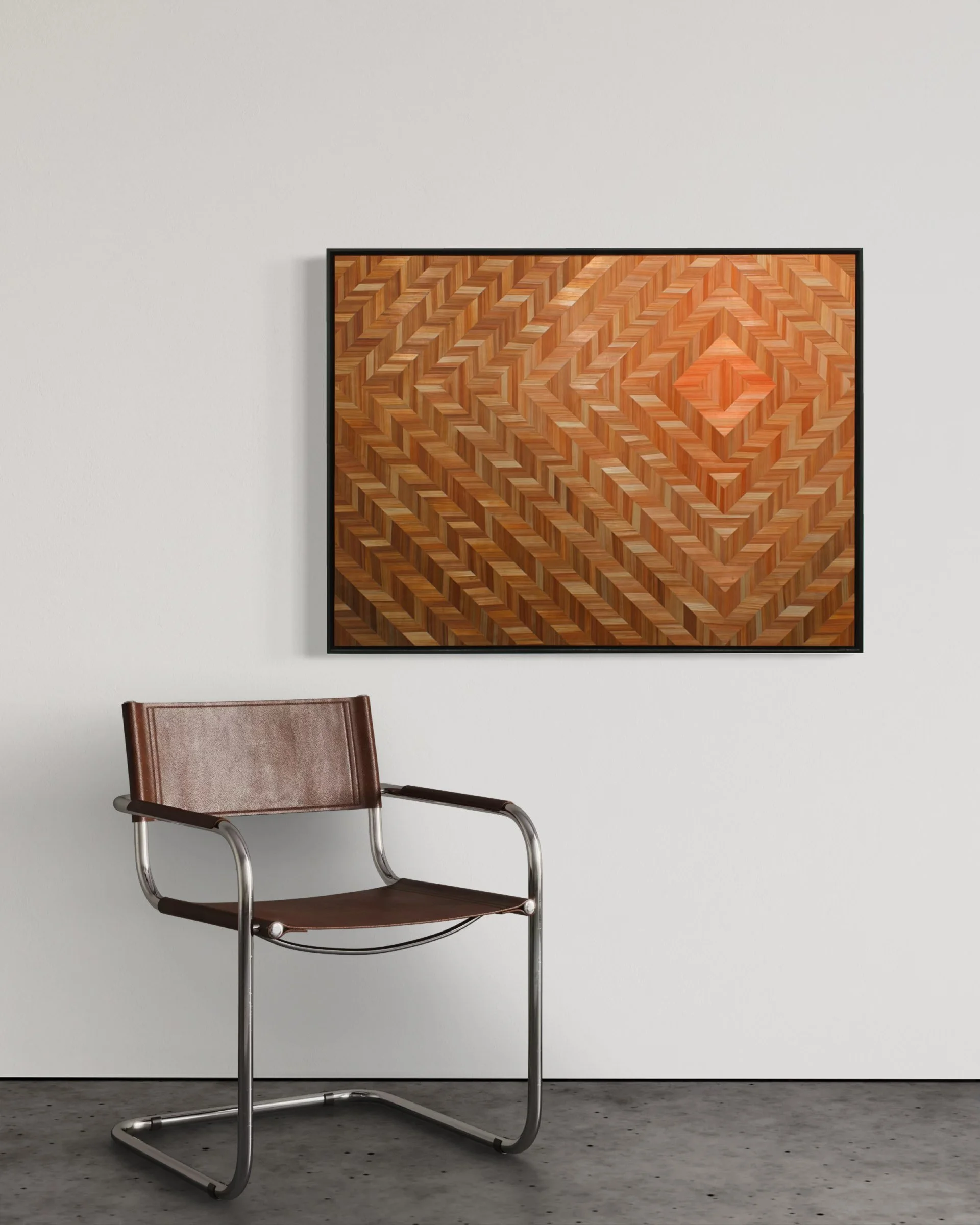 Straw marquetry artwork "Enveloped" installed on a white wall above a modern chair; 30 × 40 inch framed panel in coral and brown tones