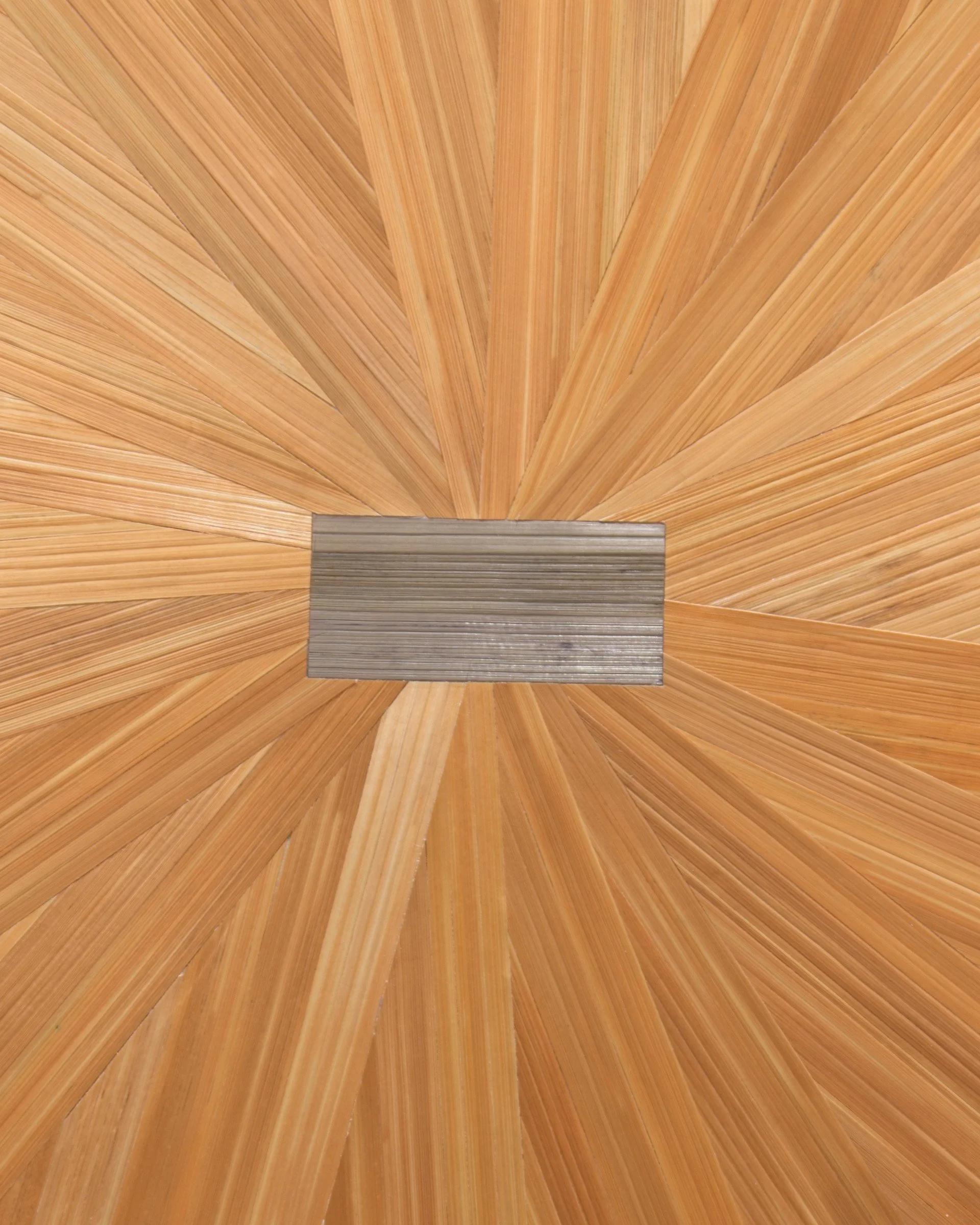 Close detail of hand-dyed rye straw in amber and burnt orange radiating from the center of a straw marquetry floral pinwheel; organic fiber texture and silken sheen visible in the straw surface