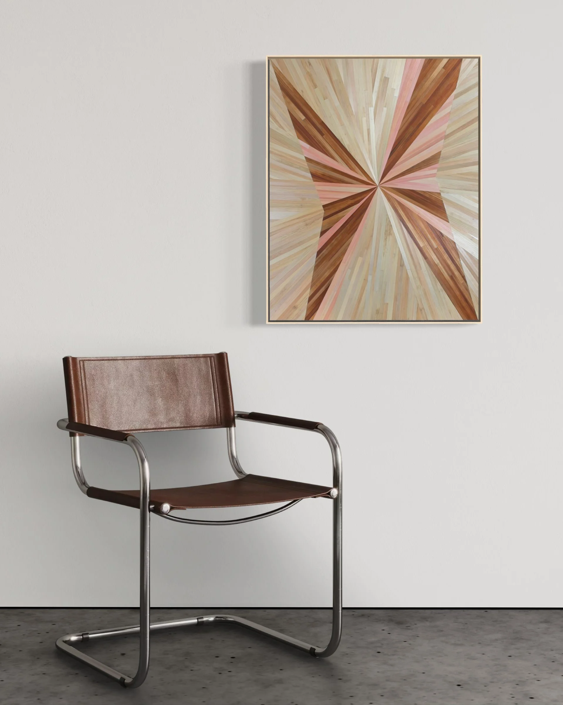 Straw marquetry artwork installed on a plain white wall above a modern chair — abstract radial burst wall art in warm pink and brown tones, float framed in maple, by New England artist Sarah Schwartz