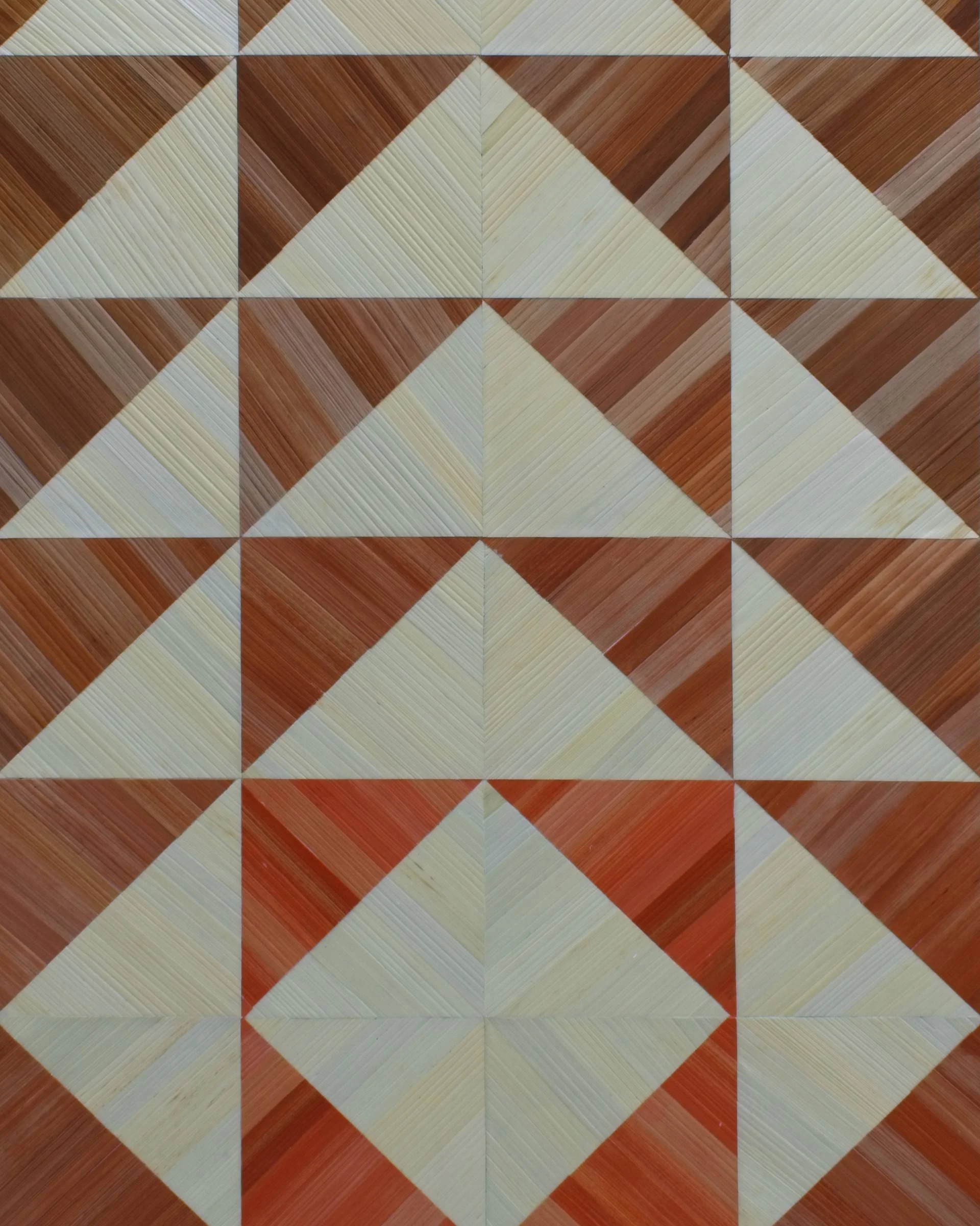 Close-up of hand-dyed rye straw triangle pattern in straw marquetry; individual straw sections in copper and ivory laid at opposing angles, showing natural straw grain and surface sheen