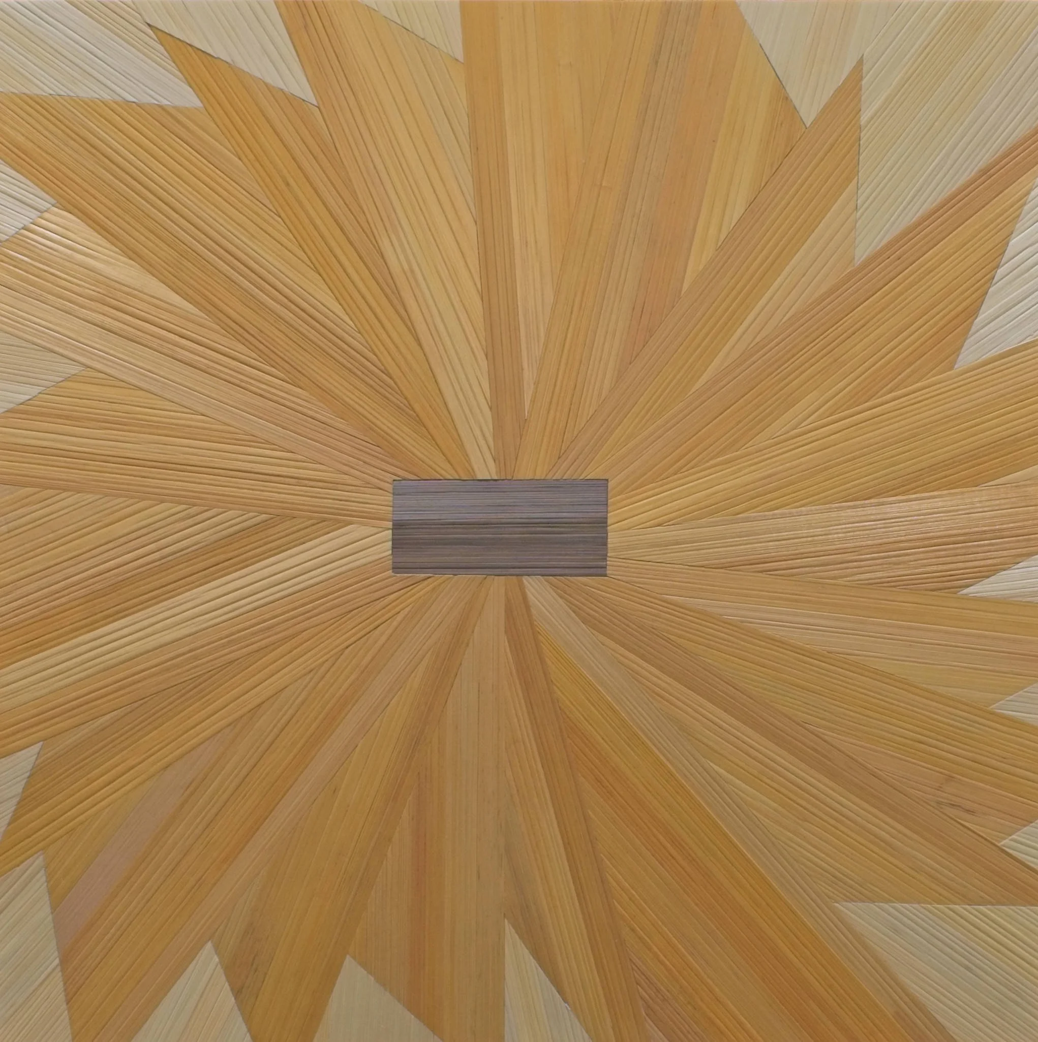 Straw marquetry fiber artwork showing a pinwheel sunburst pattern in dyed golden yellow rye straw with a gray-brown horizontal center rectangle and natural straw ground at the corners; 12×12in