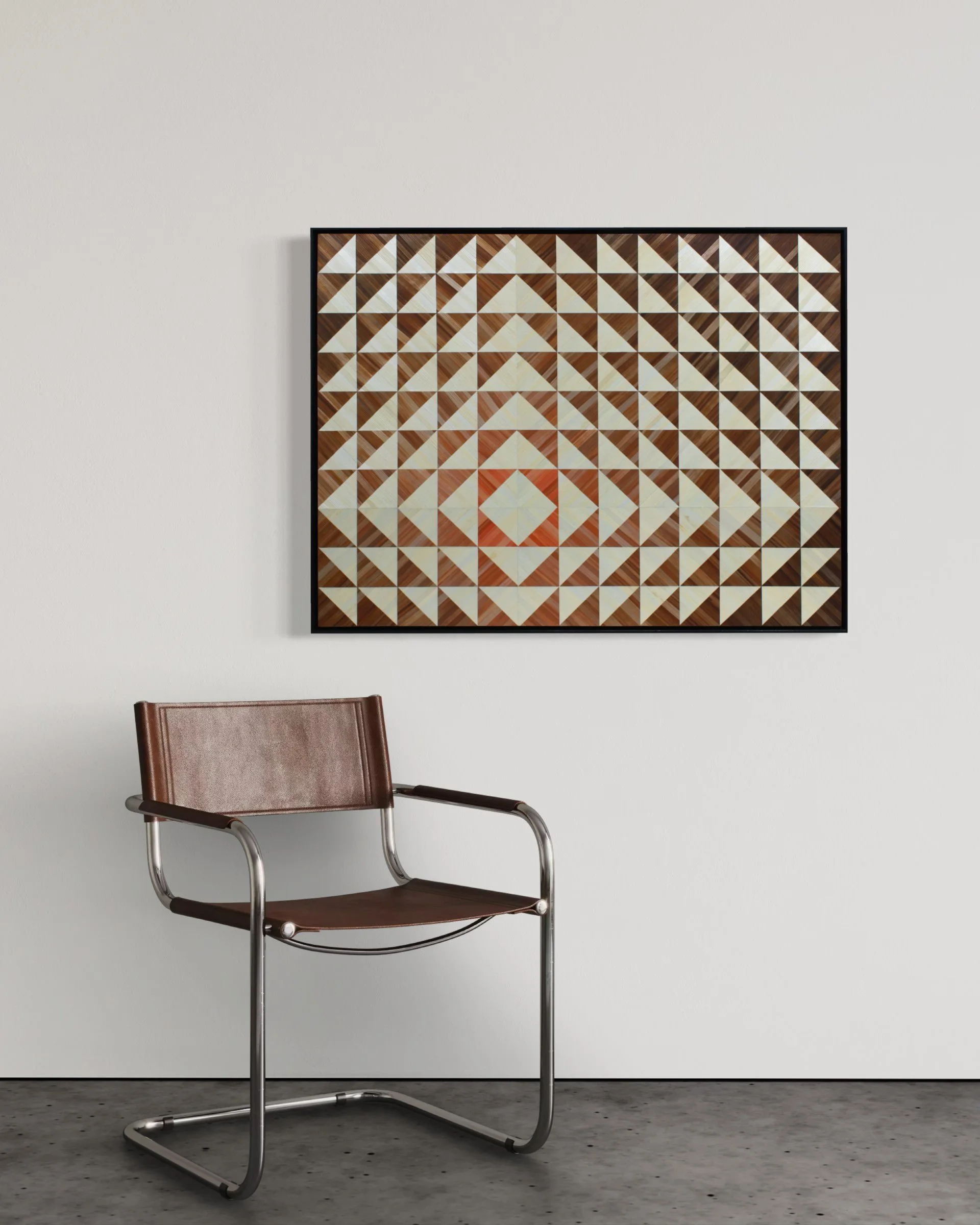 Abstract straw marquetry artwork "Enter the Sun" installed on a plain wall above a modern chair; 40 × 30 inch geometric panel in warm coral, copper, rust, and ivory tones