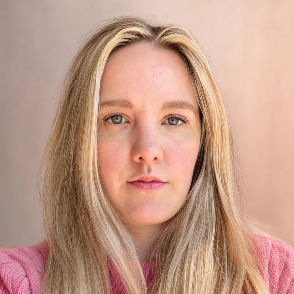 A close-up portrait of a woman with long blonde hair, fair skin, and green eyes, wearing a pink sweater with a neutral expression, against a soft beige background.