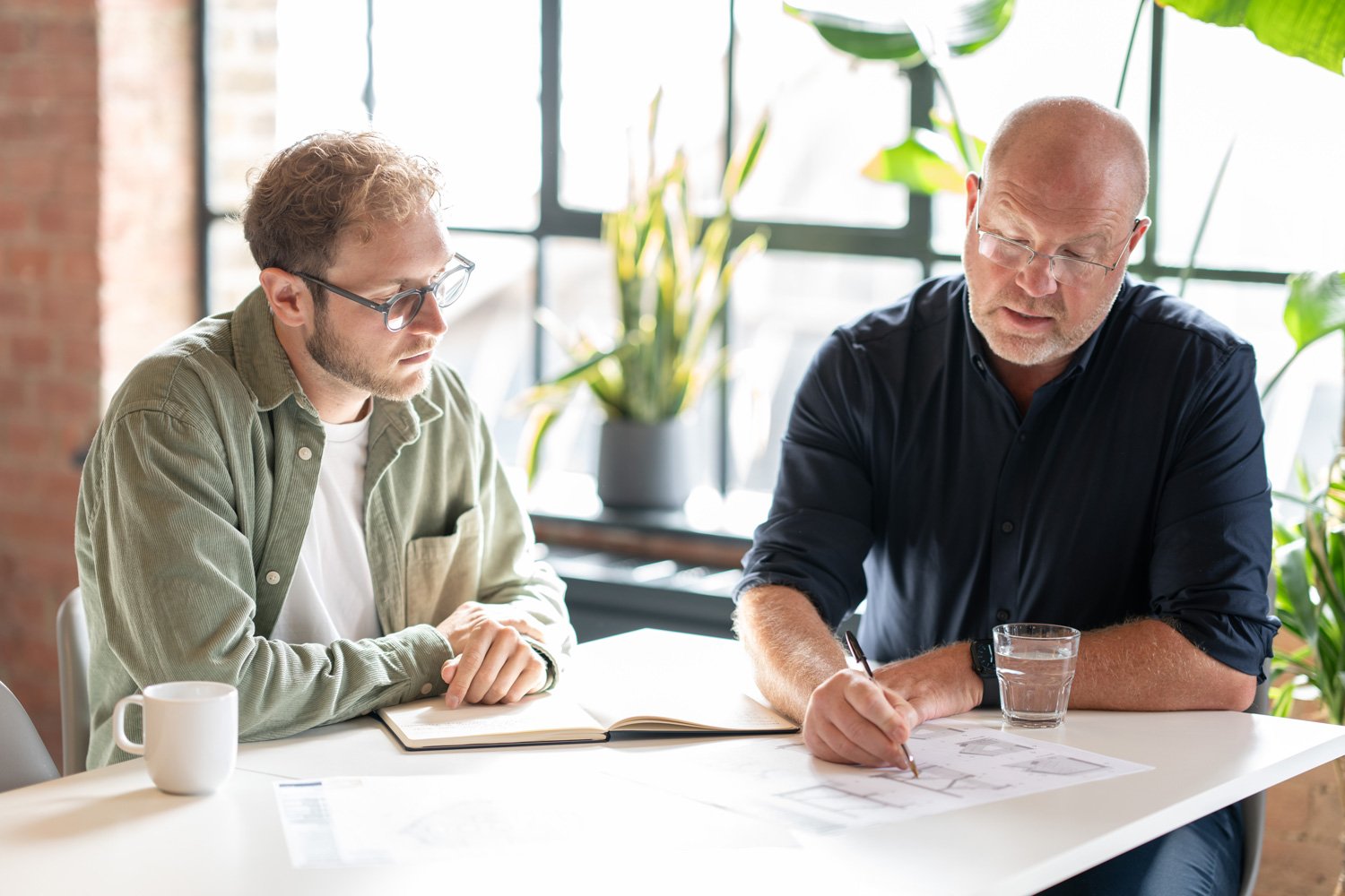Two Form Structural Design colleagues discuss structural plans at a table in a sunlit office.